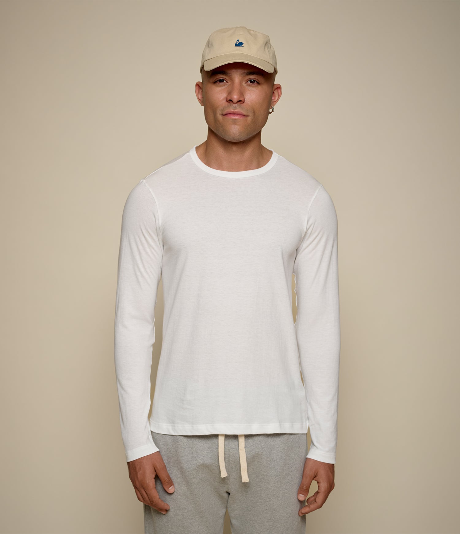Man wearing a white loopwheeled long-sleeve shirt and gray pants against a beige background
