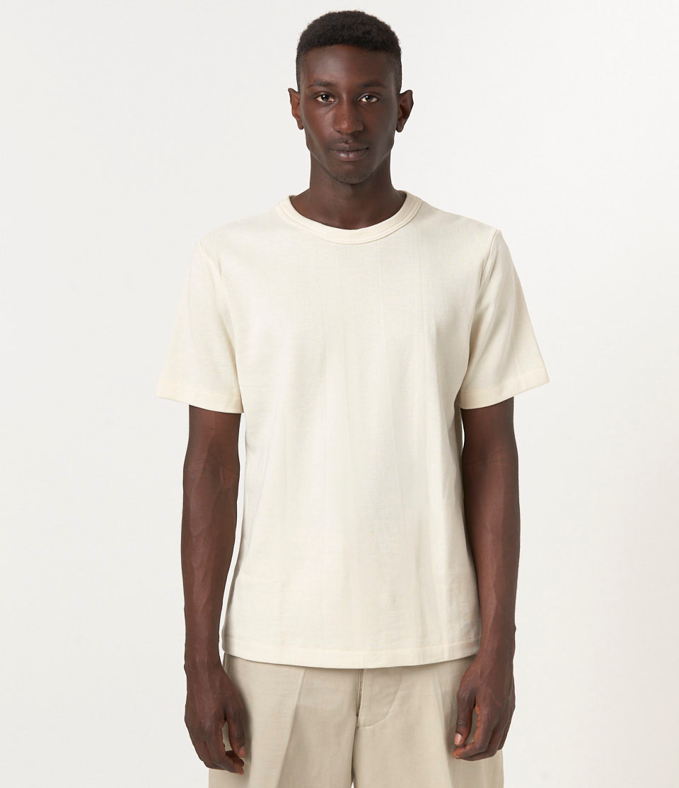 A person wearing a beige short-sleeved loopwheeled pikée T-shirt with a round neckline.