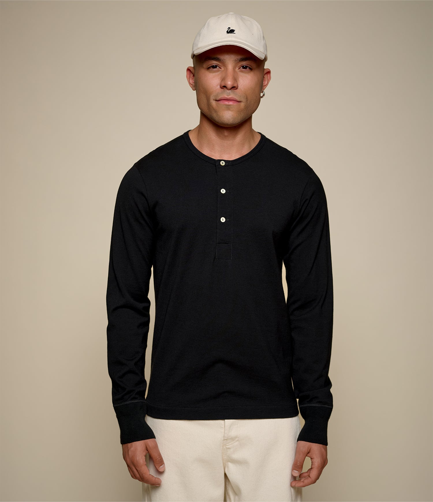 Man wearing a black long-sleeve henley shirt and beige cap against a beige background