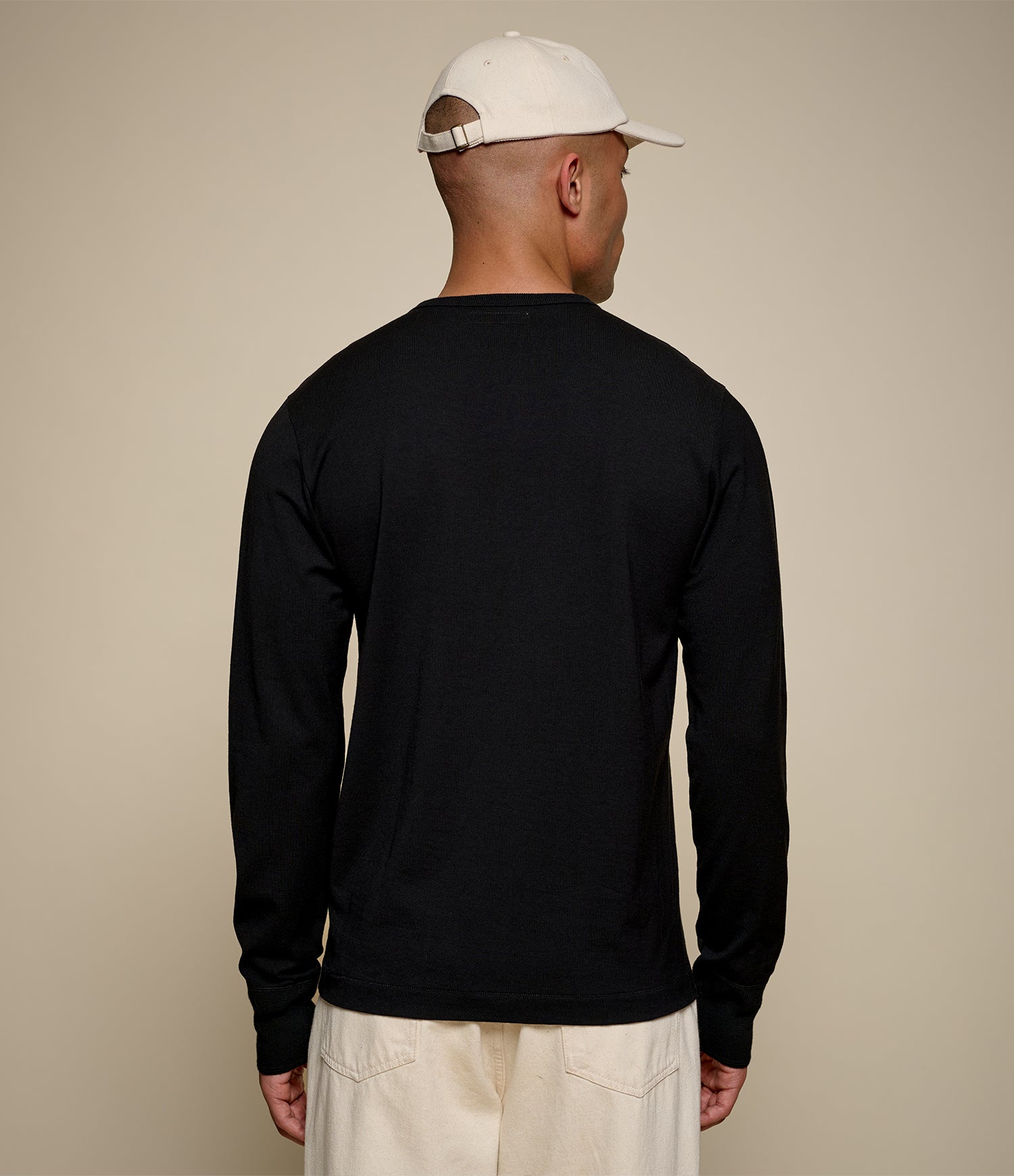 Man wearing a black long-sleeve shirt and beige cap on a beige background