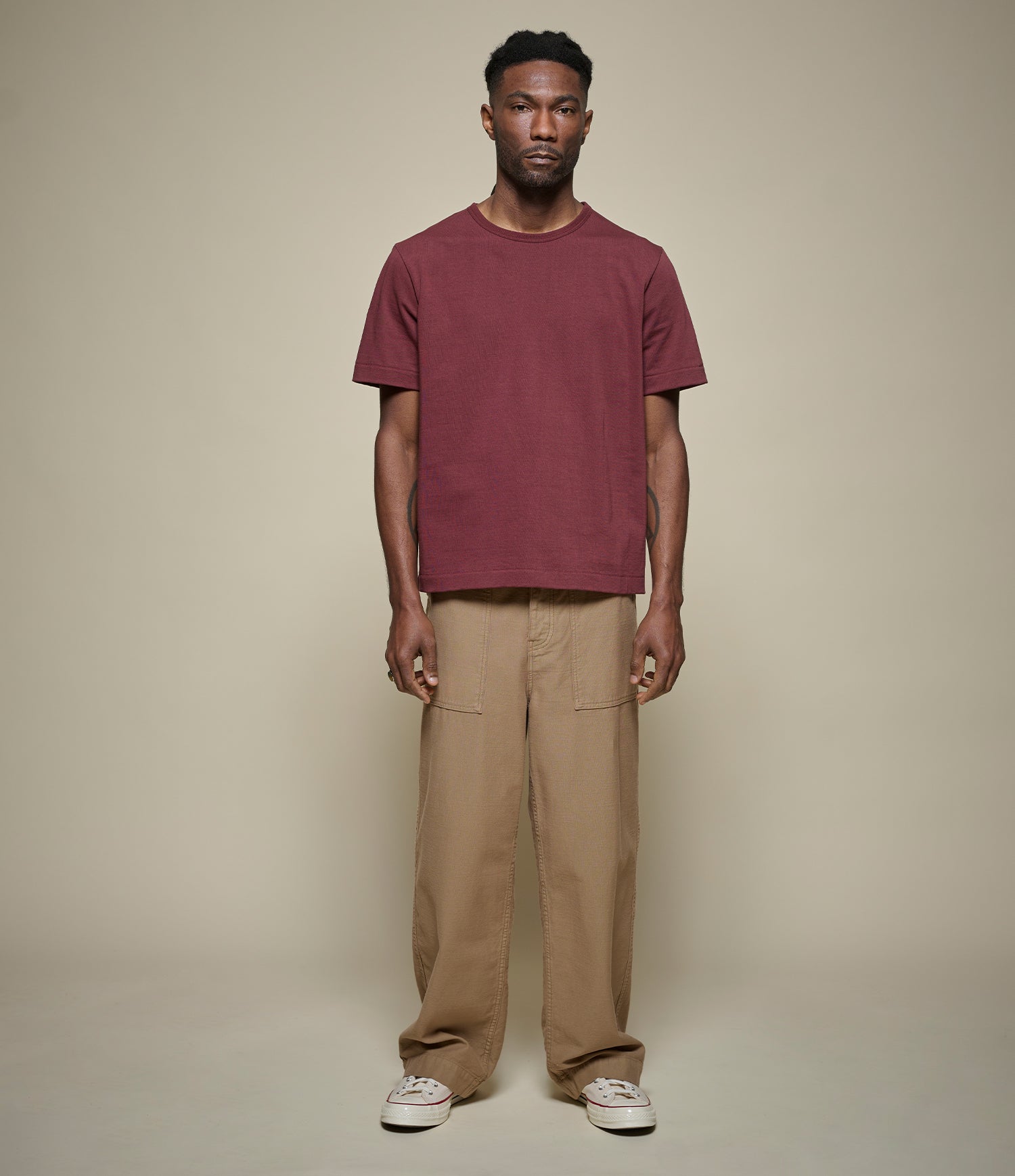 Man wearing a cropped maroon t-shirt and beige fatigue pants against a plain background