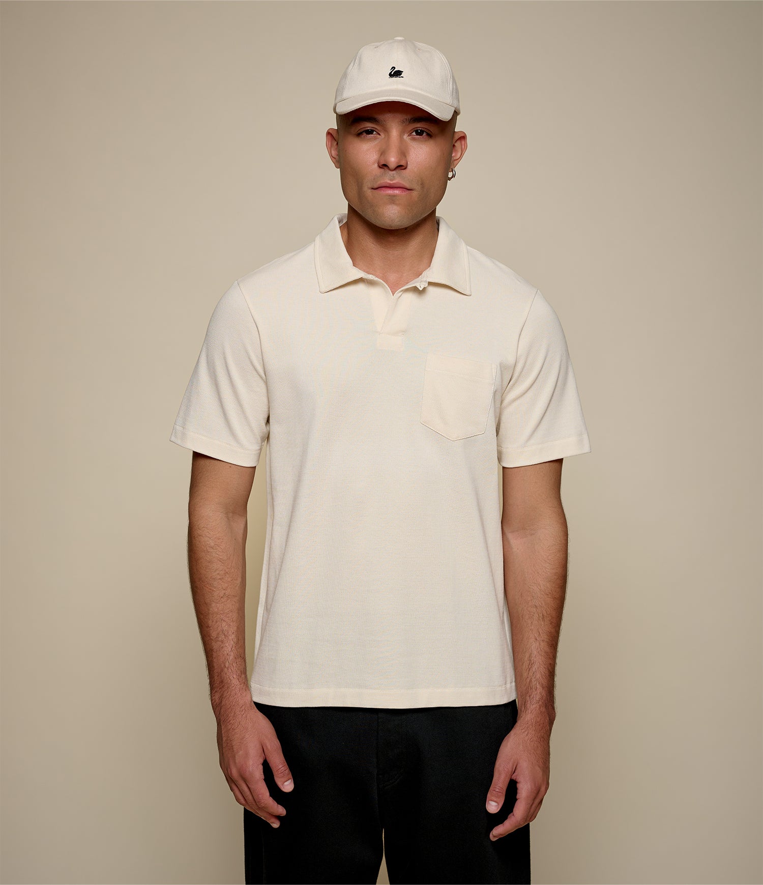 Man wearing a beige loopwheeled pikée polo shirt and cap against a beige background