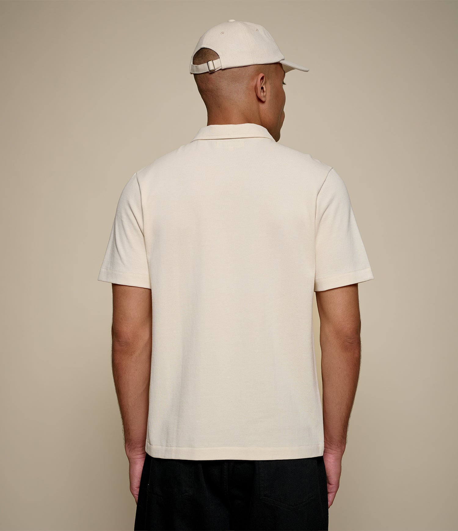 Man wearing a beige loopwheeled pikée polo shirt and cap from behind on a beige background