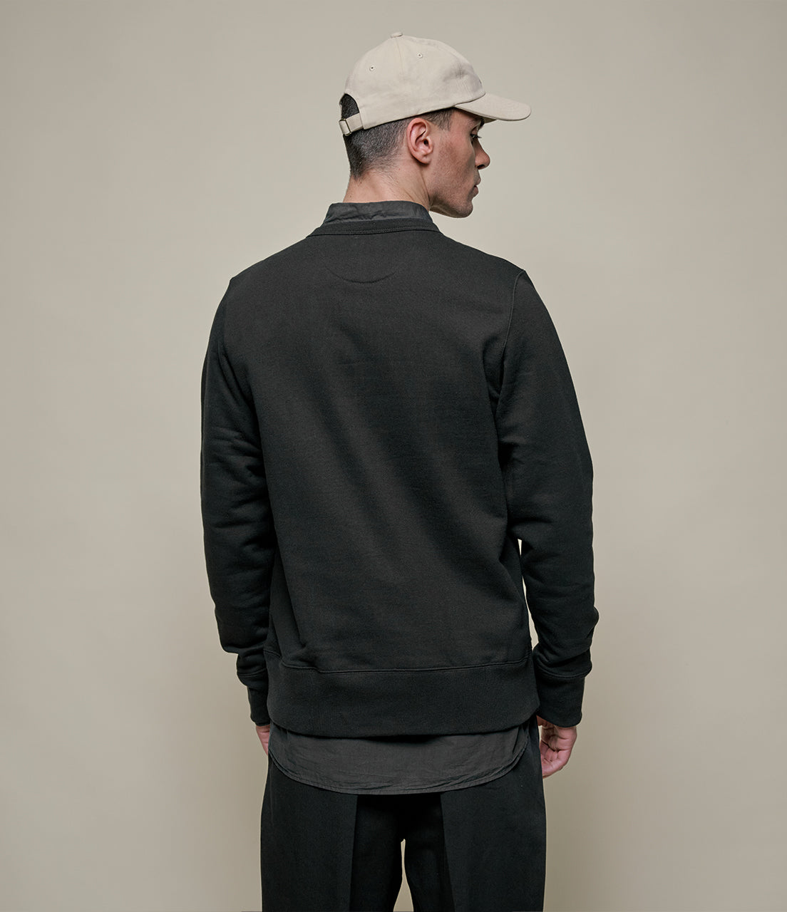 Man wearing a black jacket and beige cap on a plain background