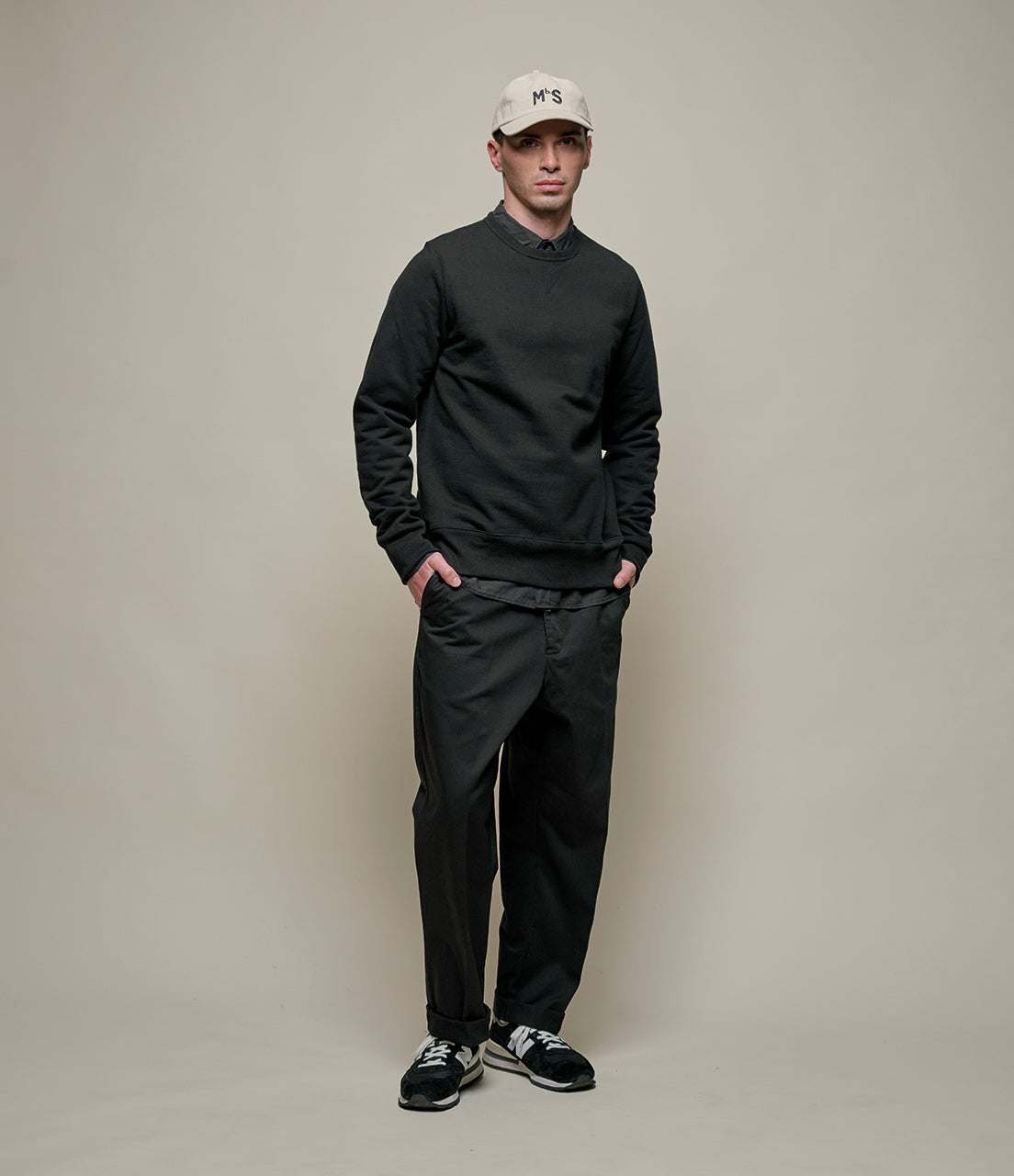 Man wearing a black outfit with a white cap against a beige background
