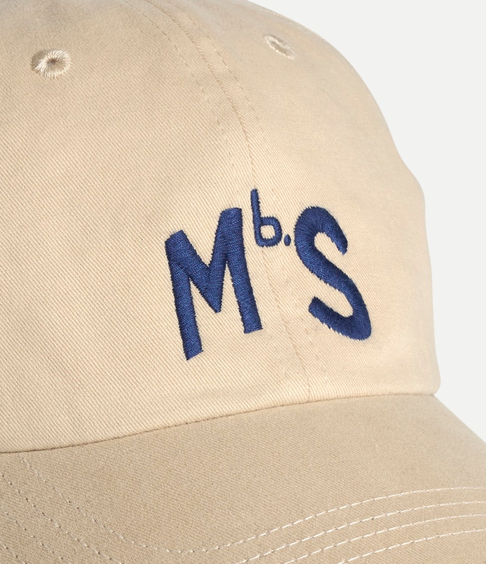Beige cap with blue 'MbS.' embroidery on a light gray background