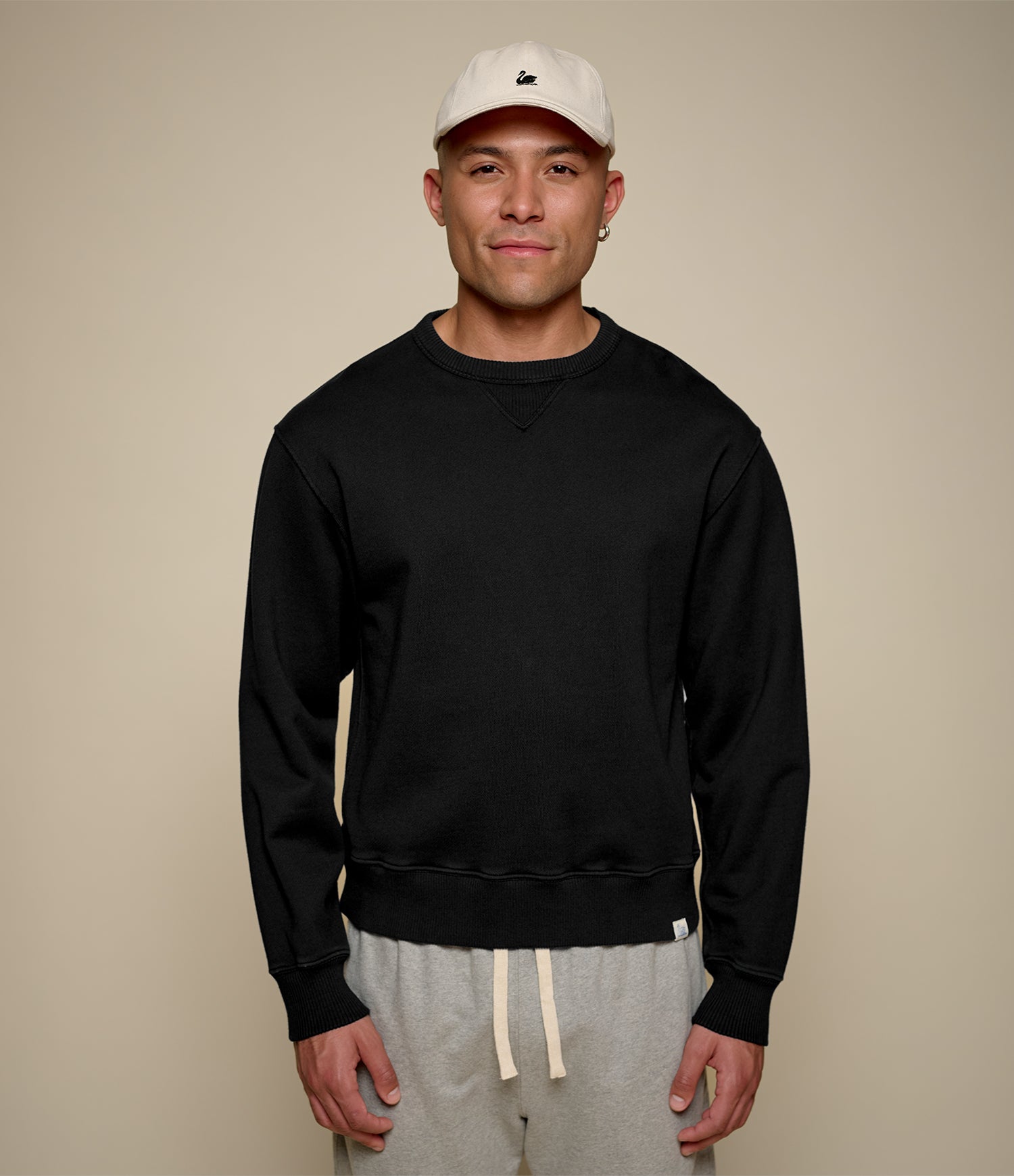 Man wearing a black fleece sweatshirt and beige cap against a beige background