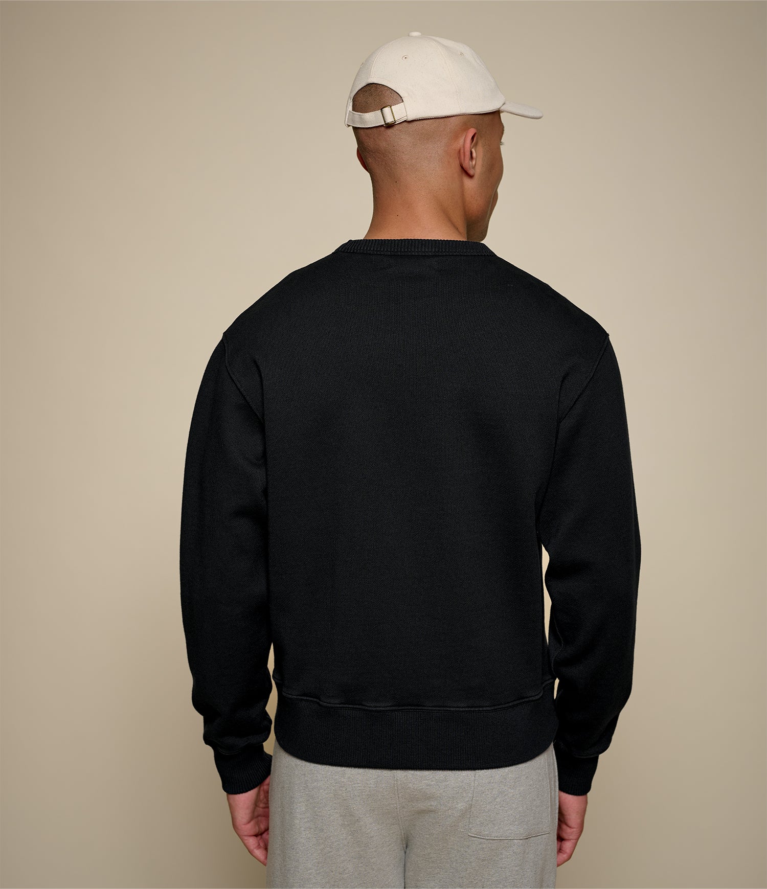 Person wearing a black fleece sweatshirt and light gray pants on a beige background