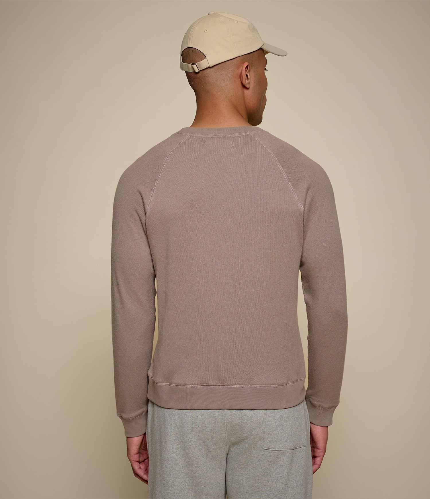 Man wearing a beige cap and brown sweatshirt against a beige background