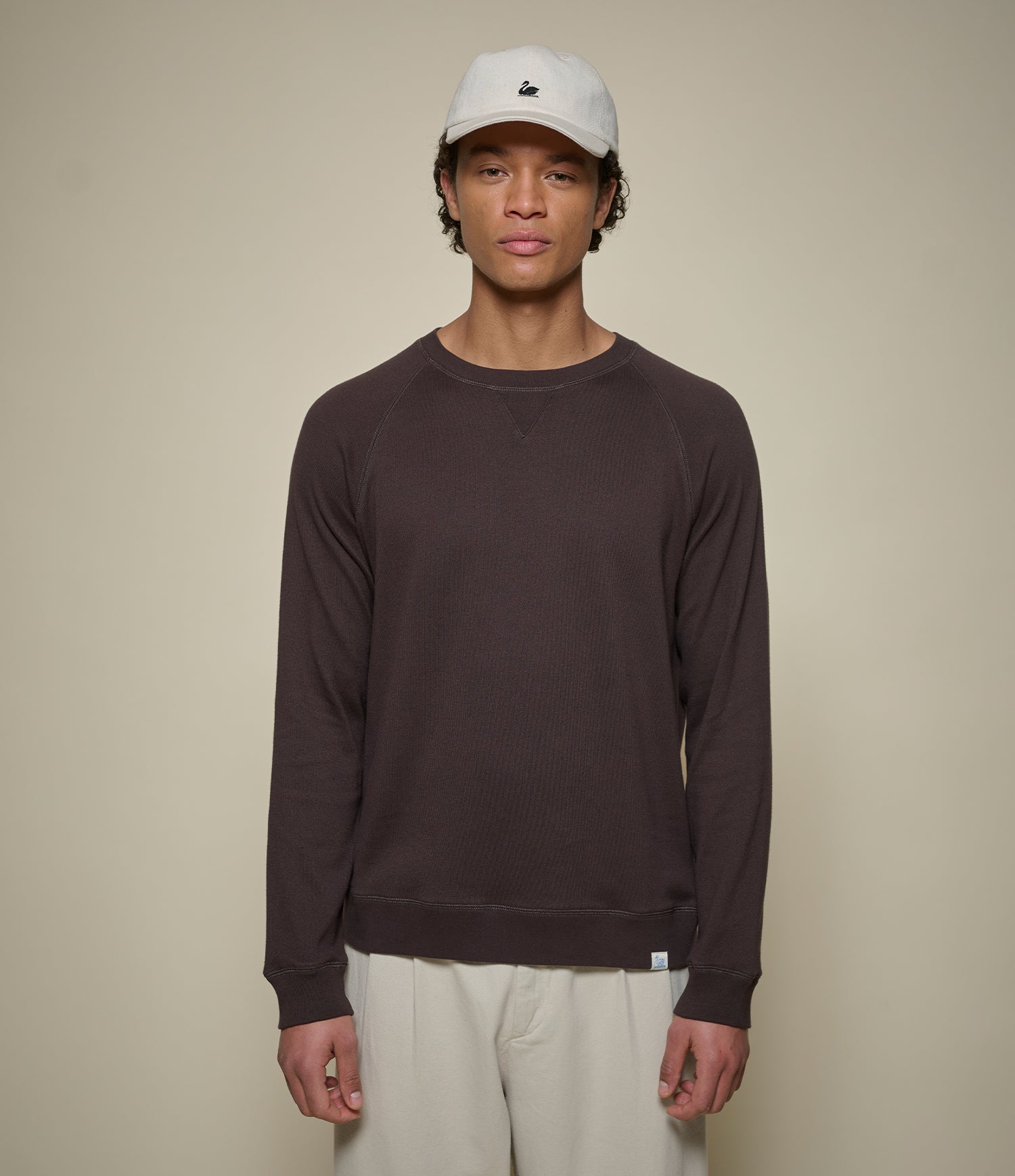 Person wearing a dark brown lightweight sweatshirt and beige cap against a plain background