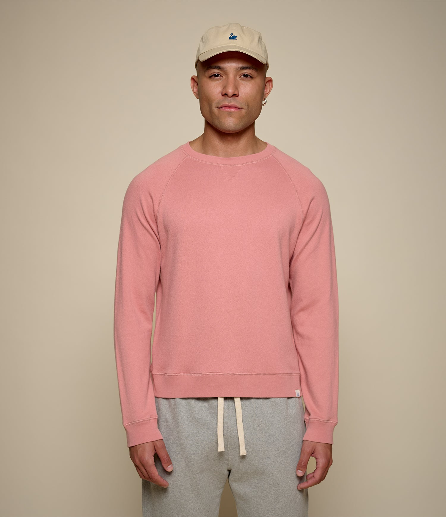 Man wearing a pink sweatshirt and gray pants against a beige background