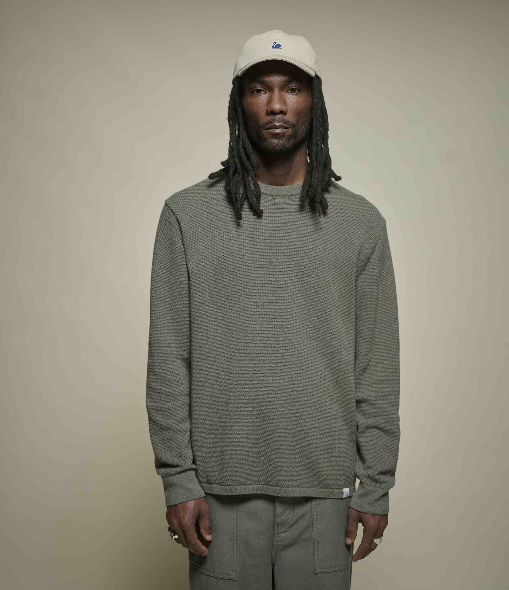 Man wearing a green lightweight sweater and beige cap against a plain background