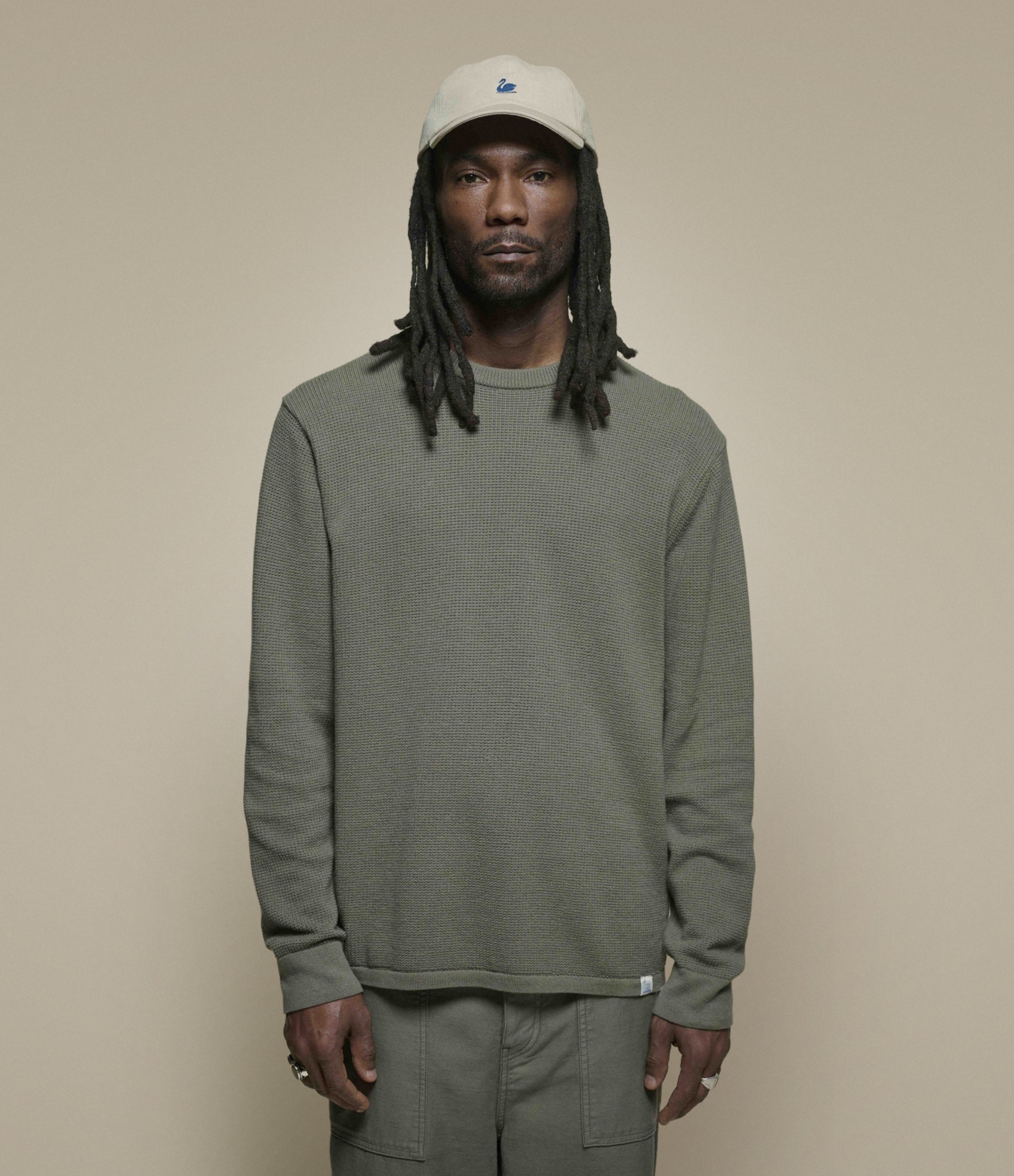 Man wearing a green lightweight sweater and beige cap against a plain background