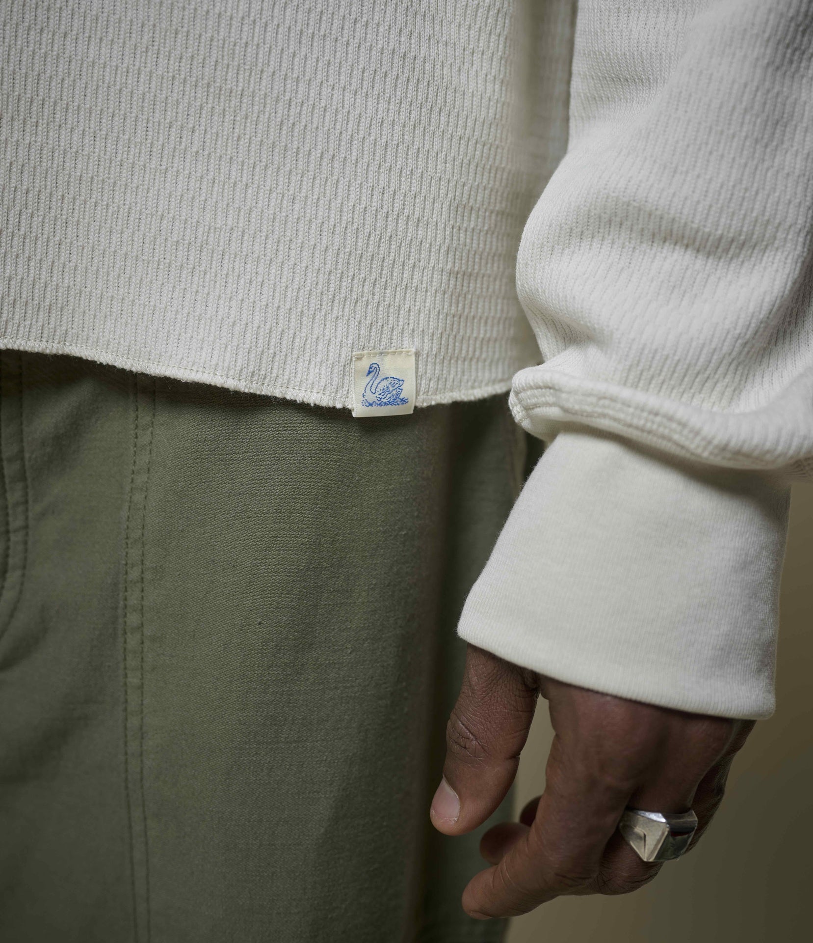 Close-up of a person wearing a cream thermal shirt and beige pants with a brand label.