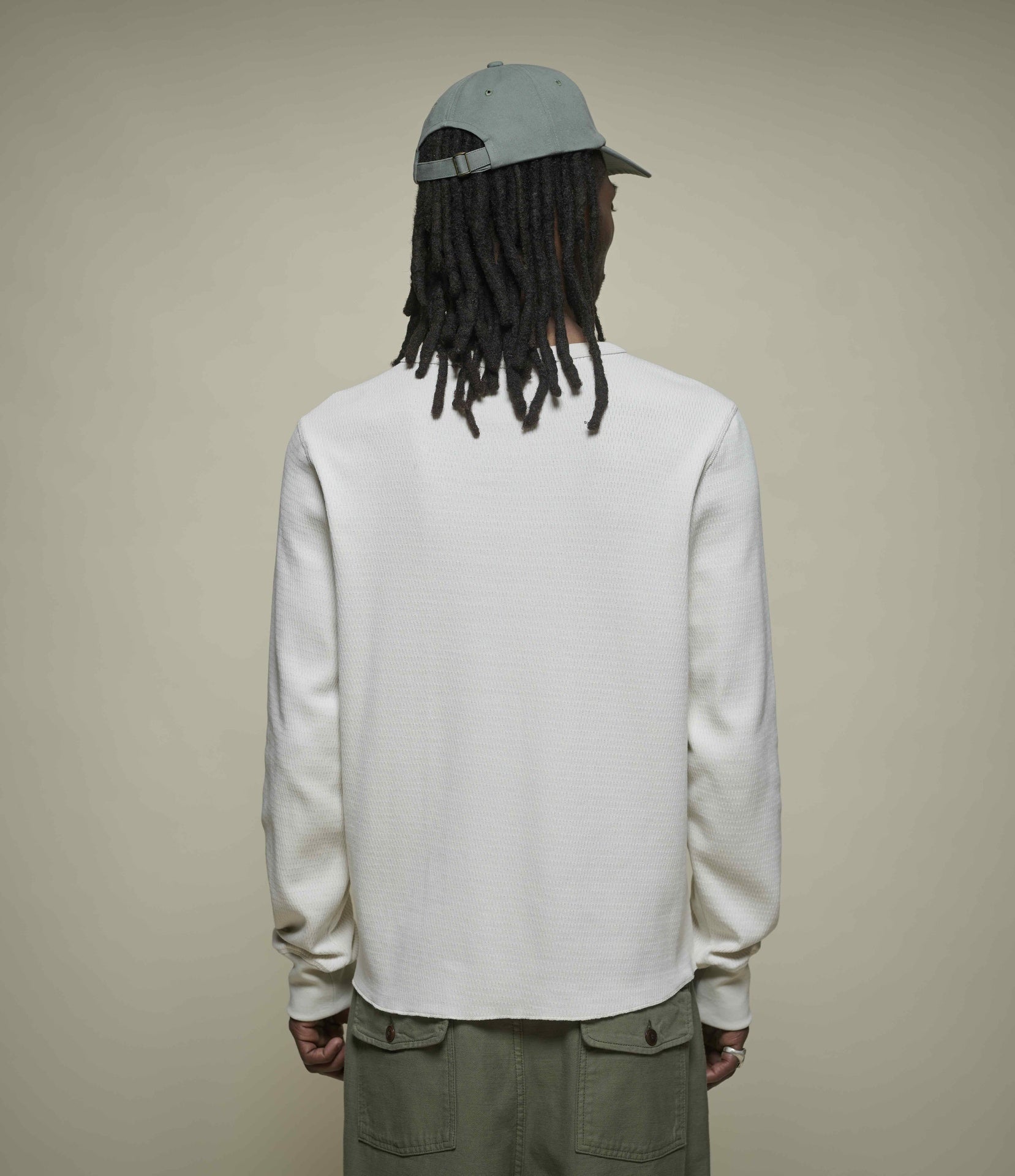 Person wearing a light-colored thermal henley and cap from behind on a beige background