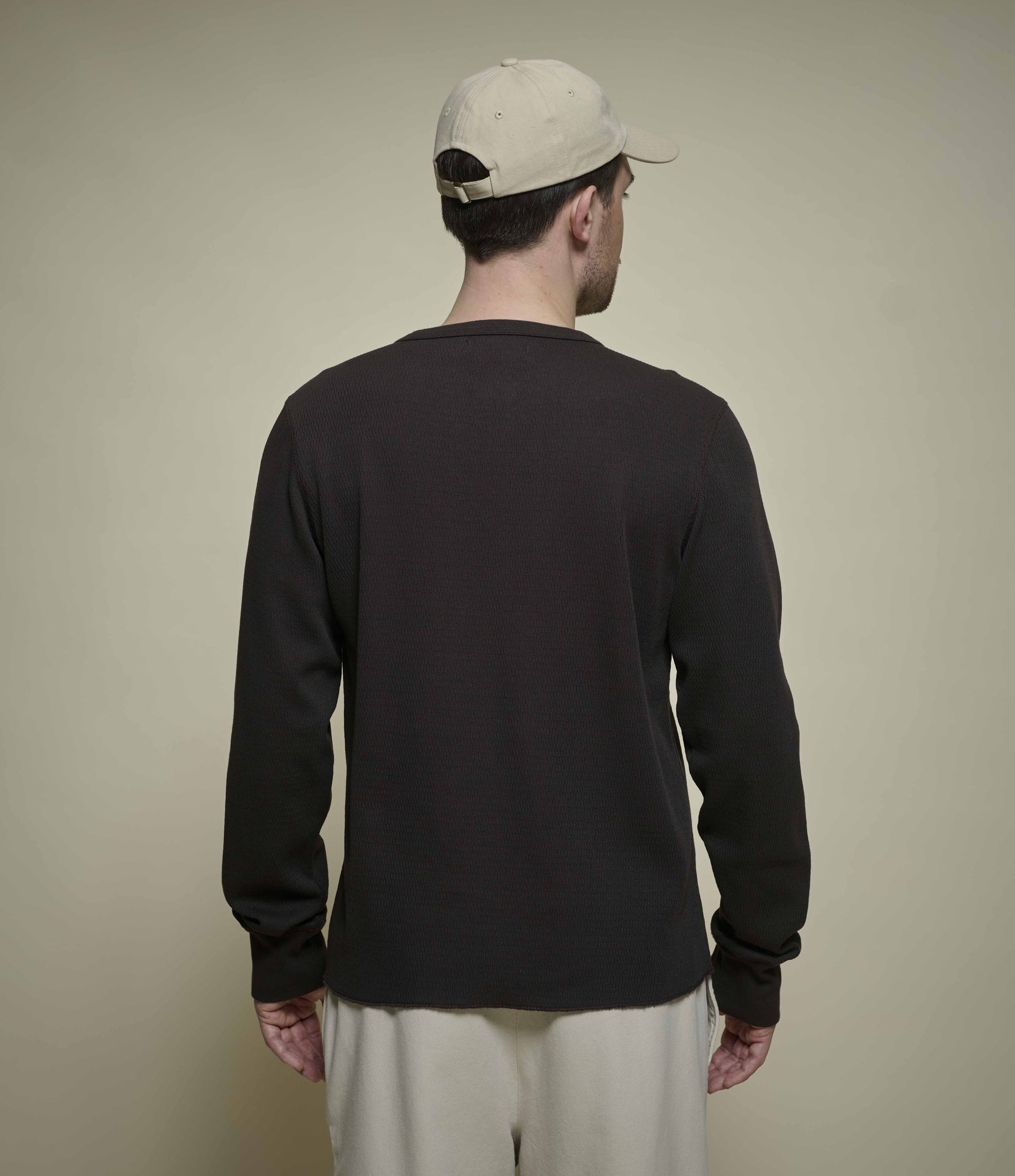 Person wearing a espresso brown long-sleeve henley shirt and beige cap from behind on a plain background