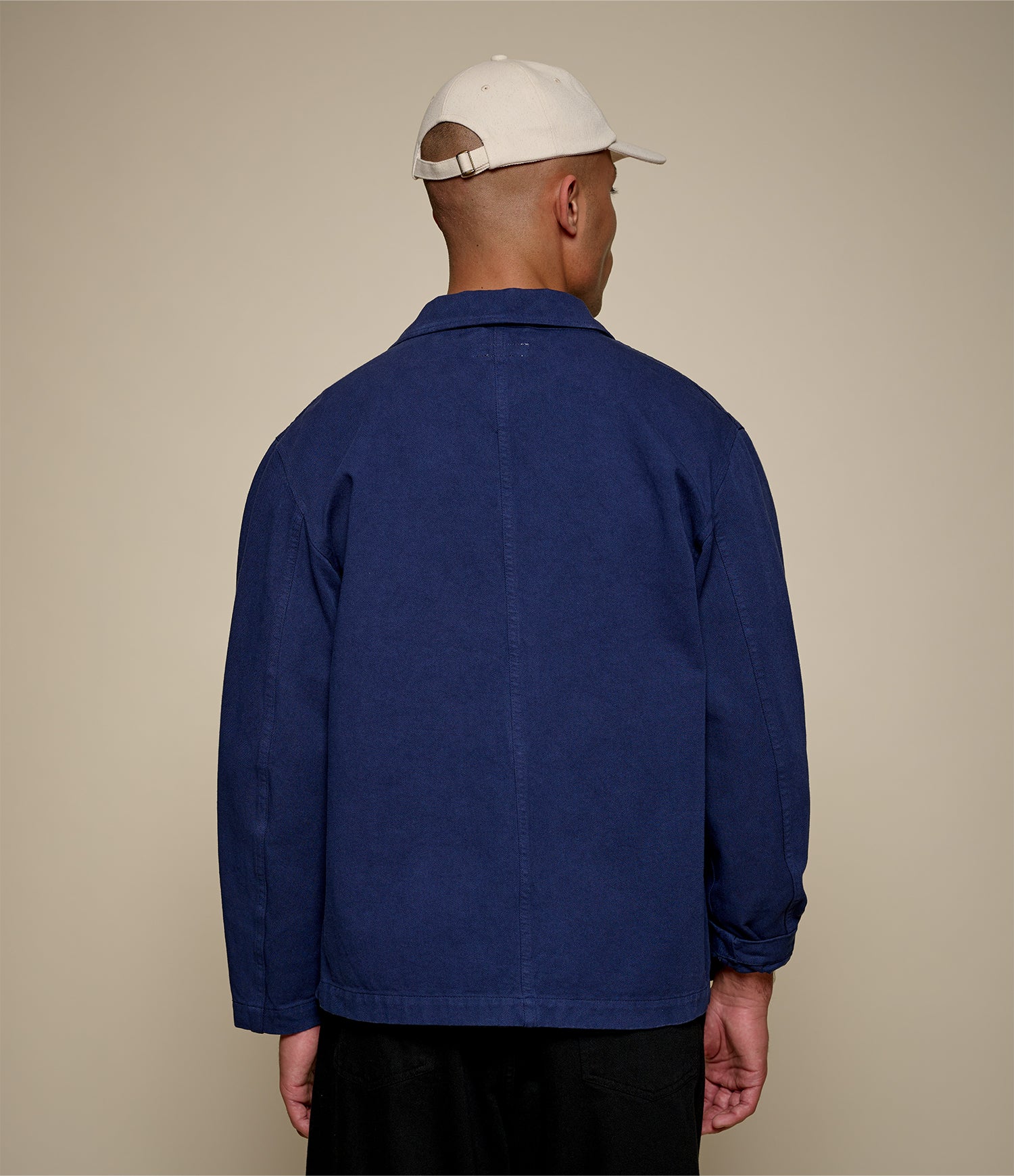 Man wearing a blue twill jacket and white cap on a beige background