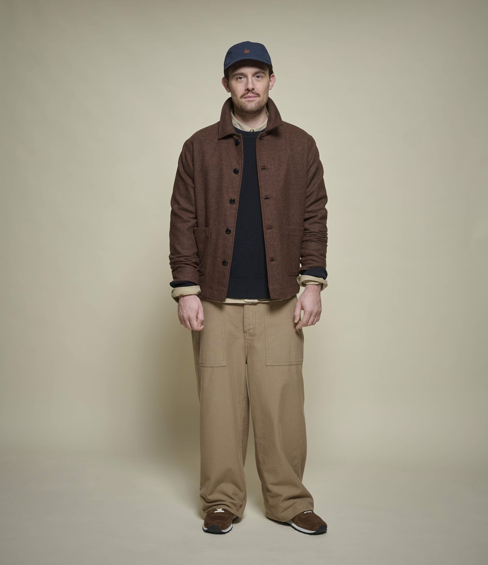 Man wearing a brown tweed jacket and beige pants against a beige background