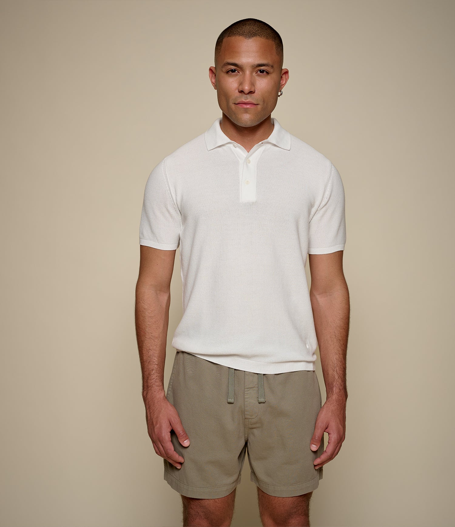 Man wearing a white knitted polo shirt and beige shorts against a beige background