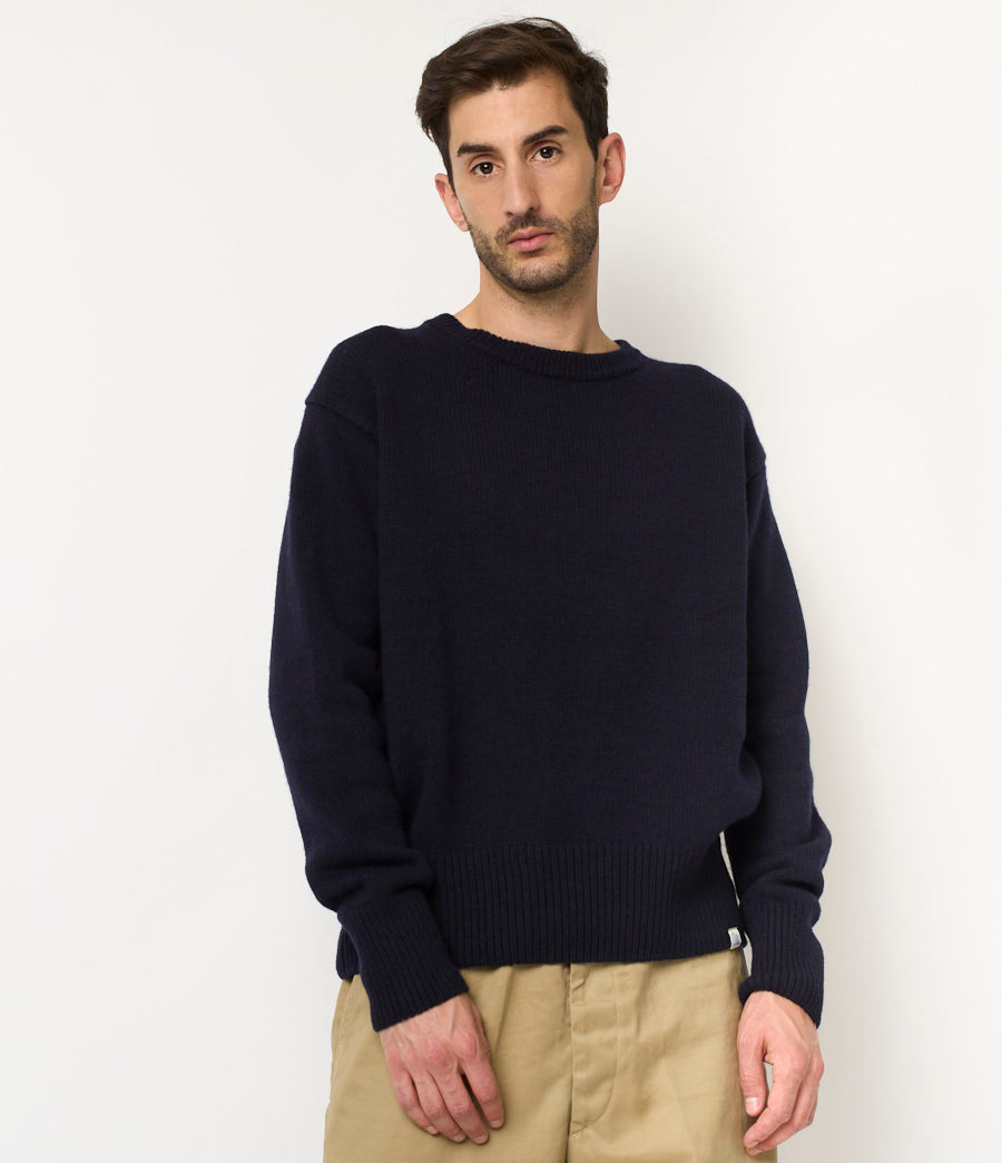 Man wearing a navy sweater and beige pants against a white background