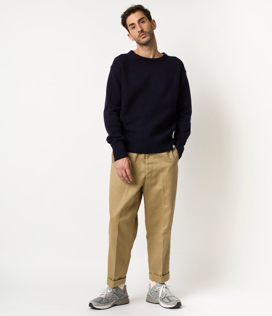Man wearing a navy sweater and beige pants on a white background