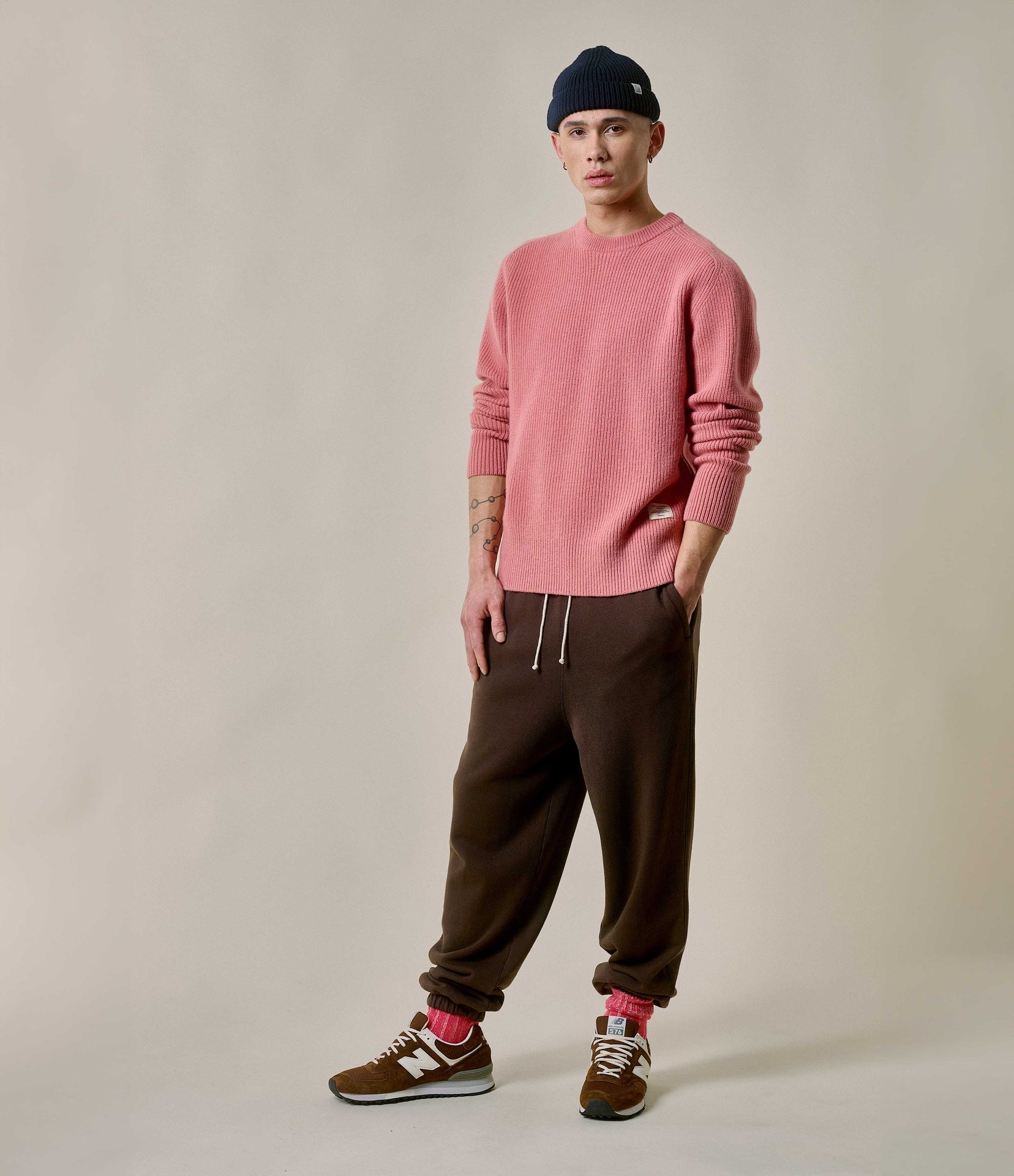 Person wearing a pink sweater and brown pants on a plain background