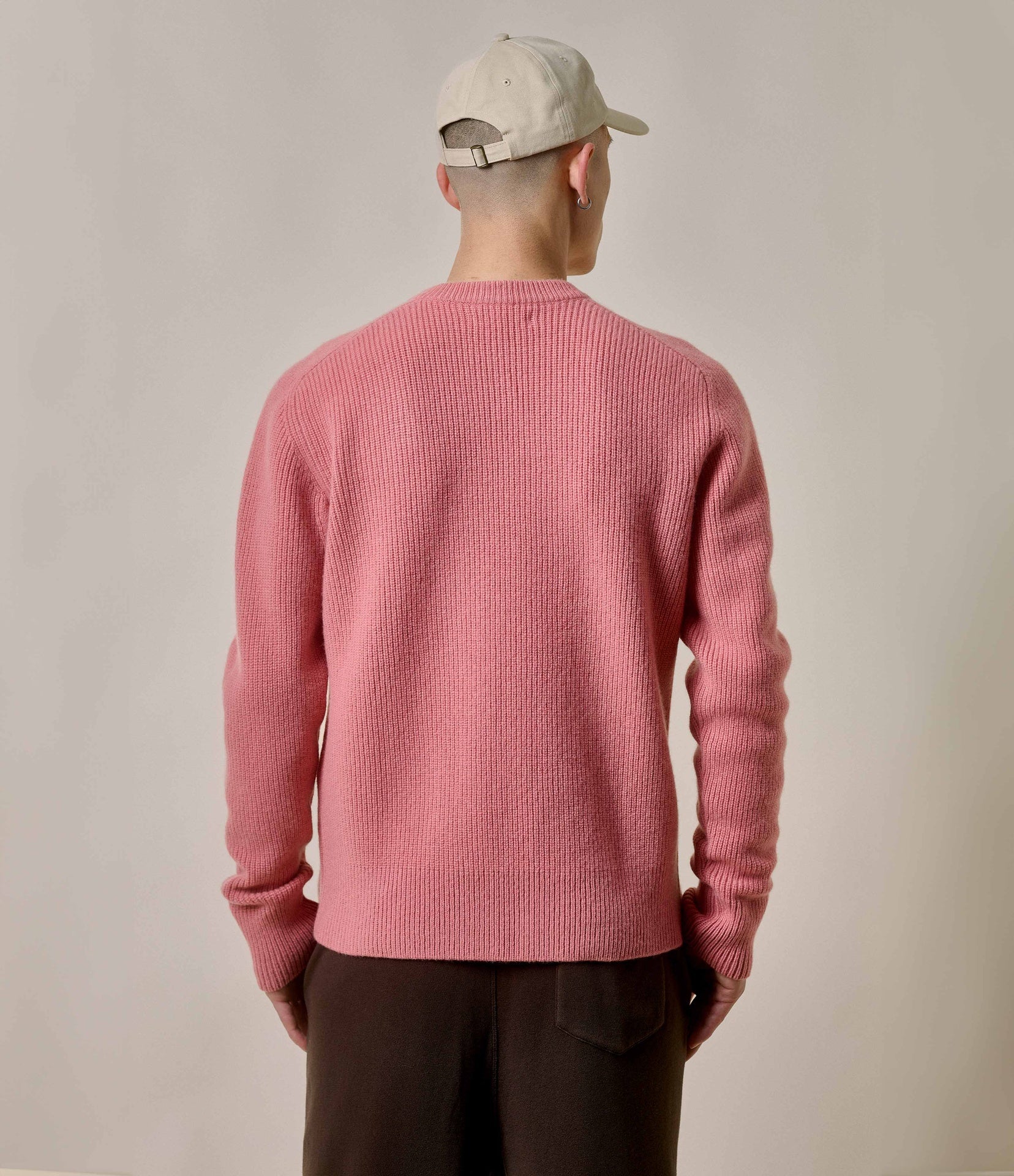 Person wearing a pink sweater and beige cap from behind on a plain background