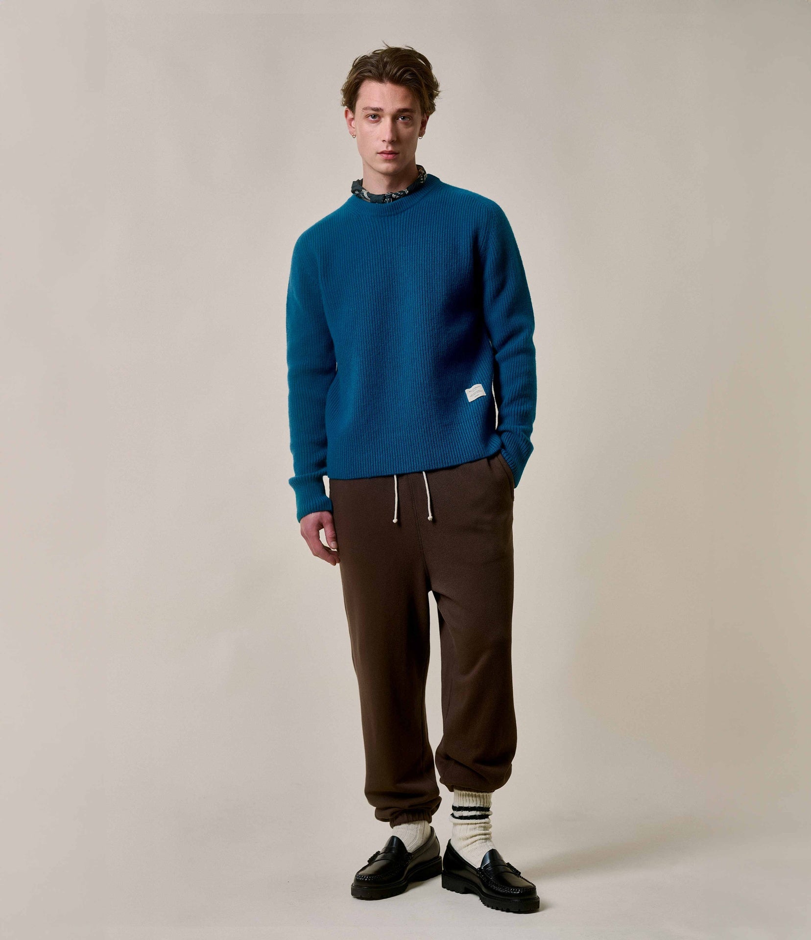 Man wearing a blue sweater and brown pants against a plain background