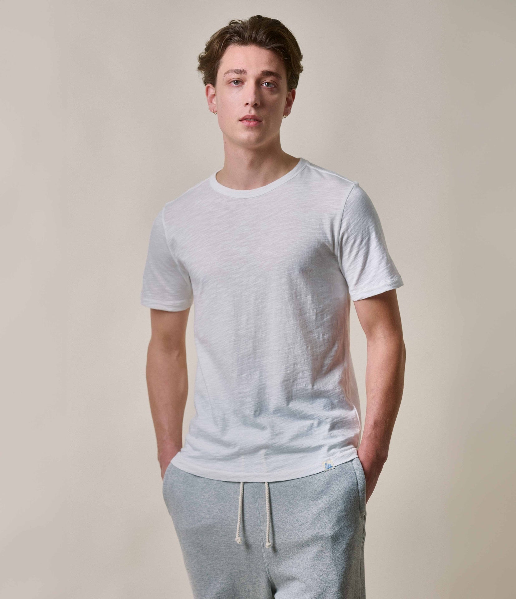 A male model wearing a white short-sleeved crew neck t-shirt and gray sweatpants.