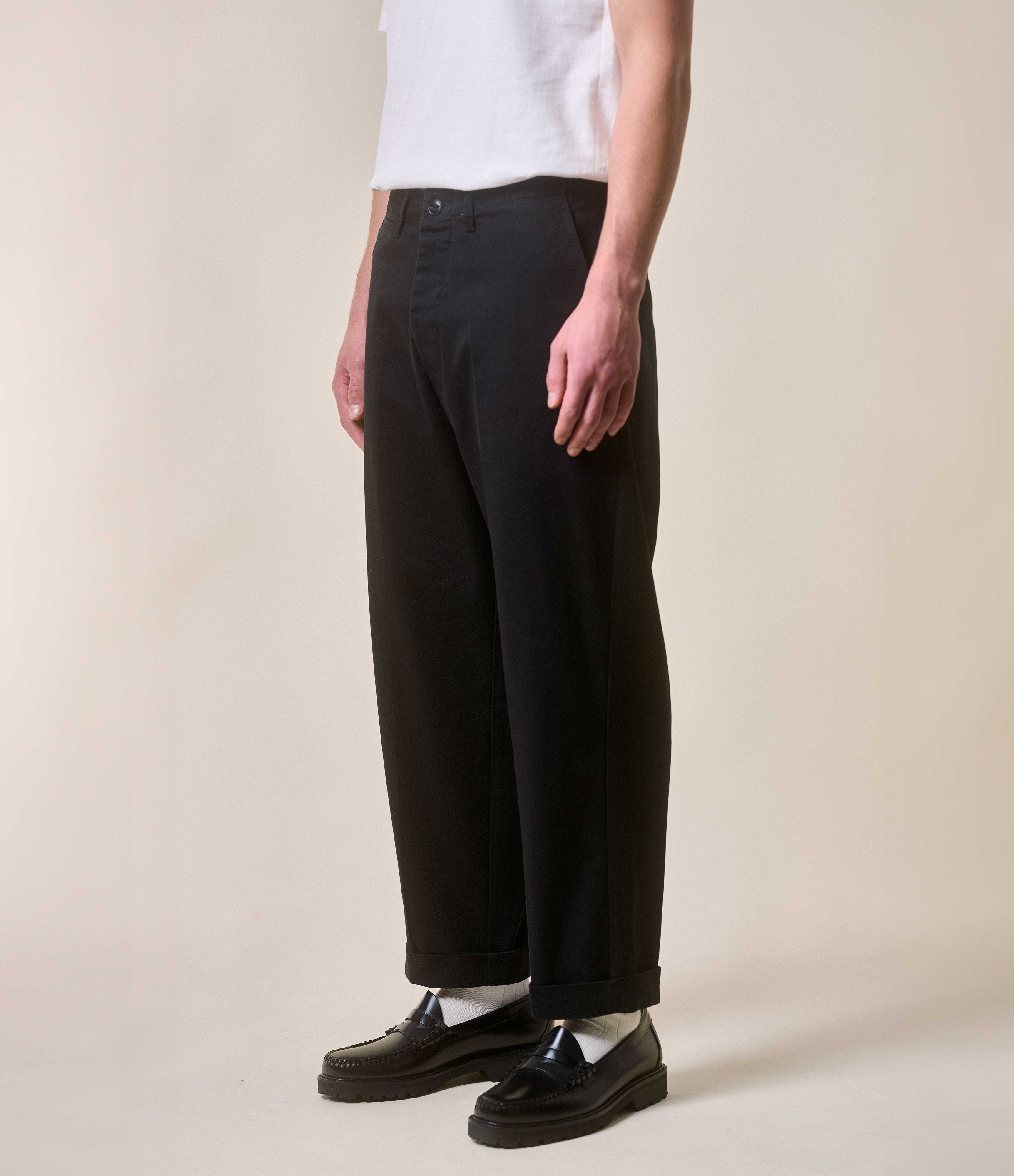 Person wearing black chinos and black shoes on a beige background