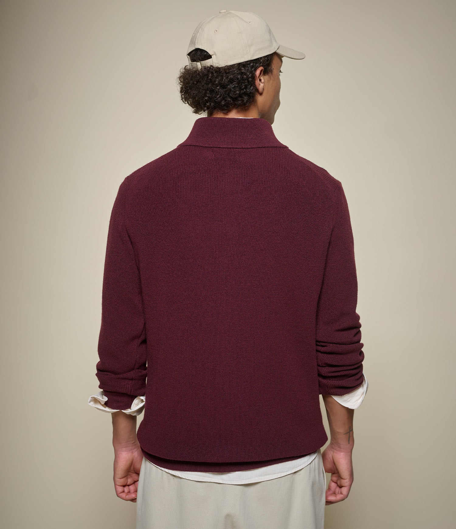 Man wearing a burgundy sweater and beige cap from behind on a plain background