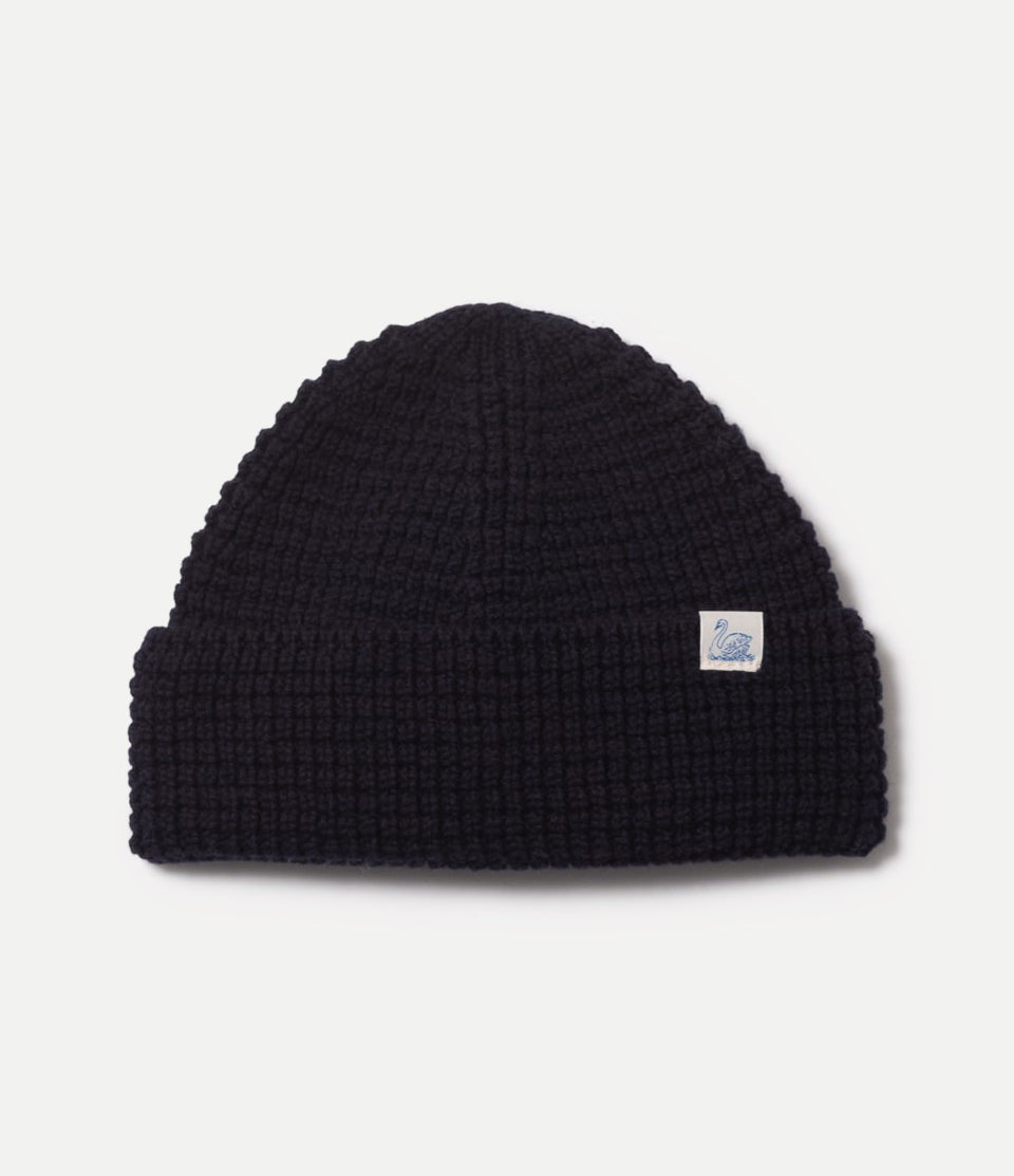 Blue waffle knit beanie with a small logo on a light gray background