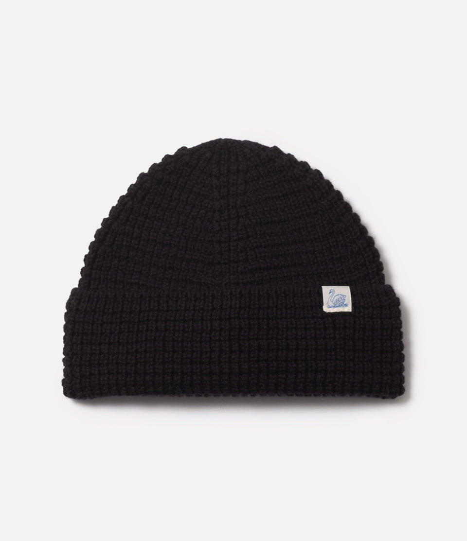 Black waffle knit beanie with a small logo on a light gray background