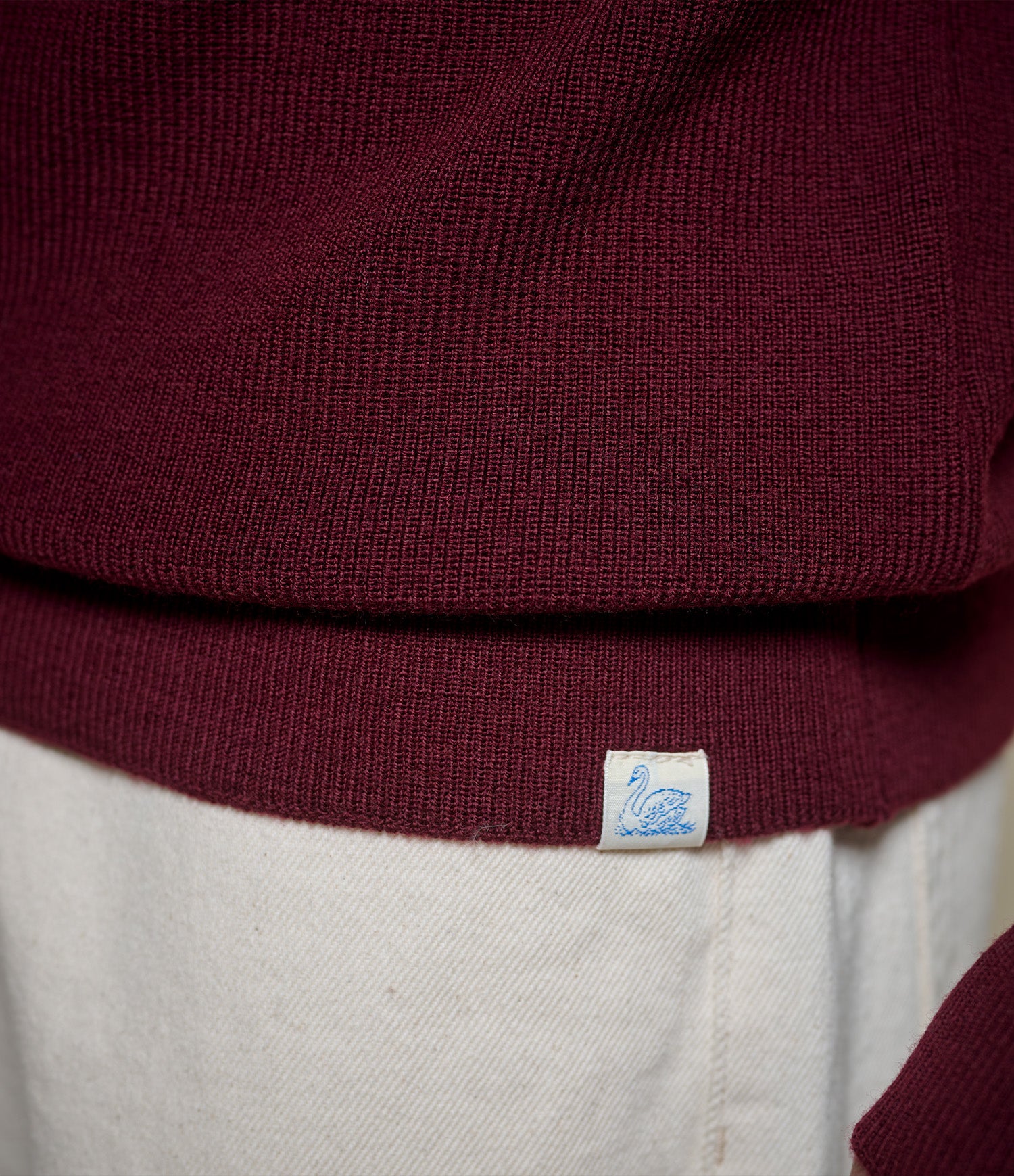 Close-up of a maroon merino wool sweater with a brand label on a neutral background