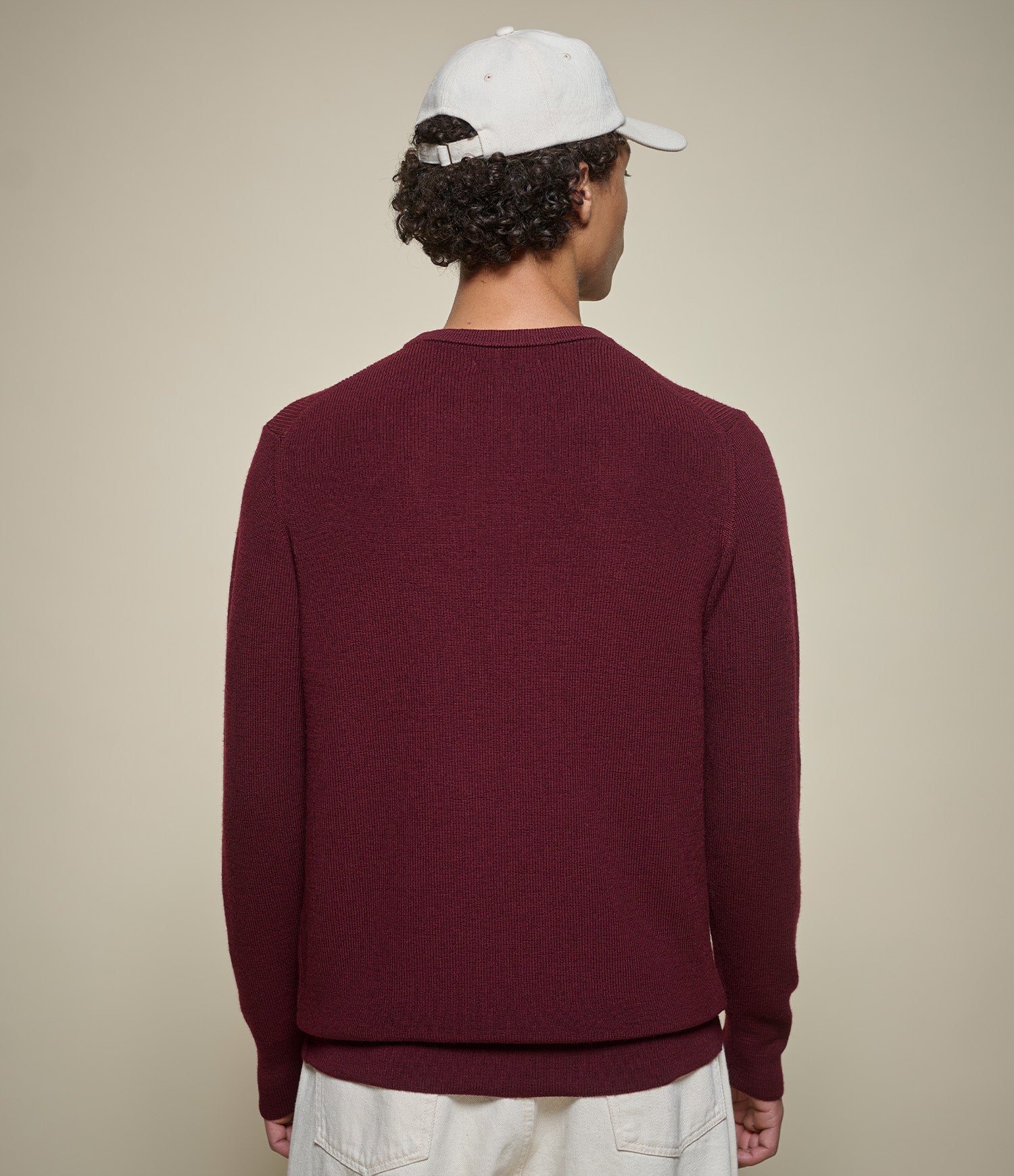 Person wearing a burgundy sweater and white cap on a beige background