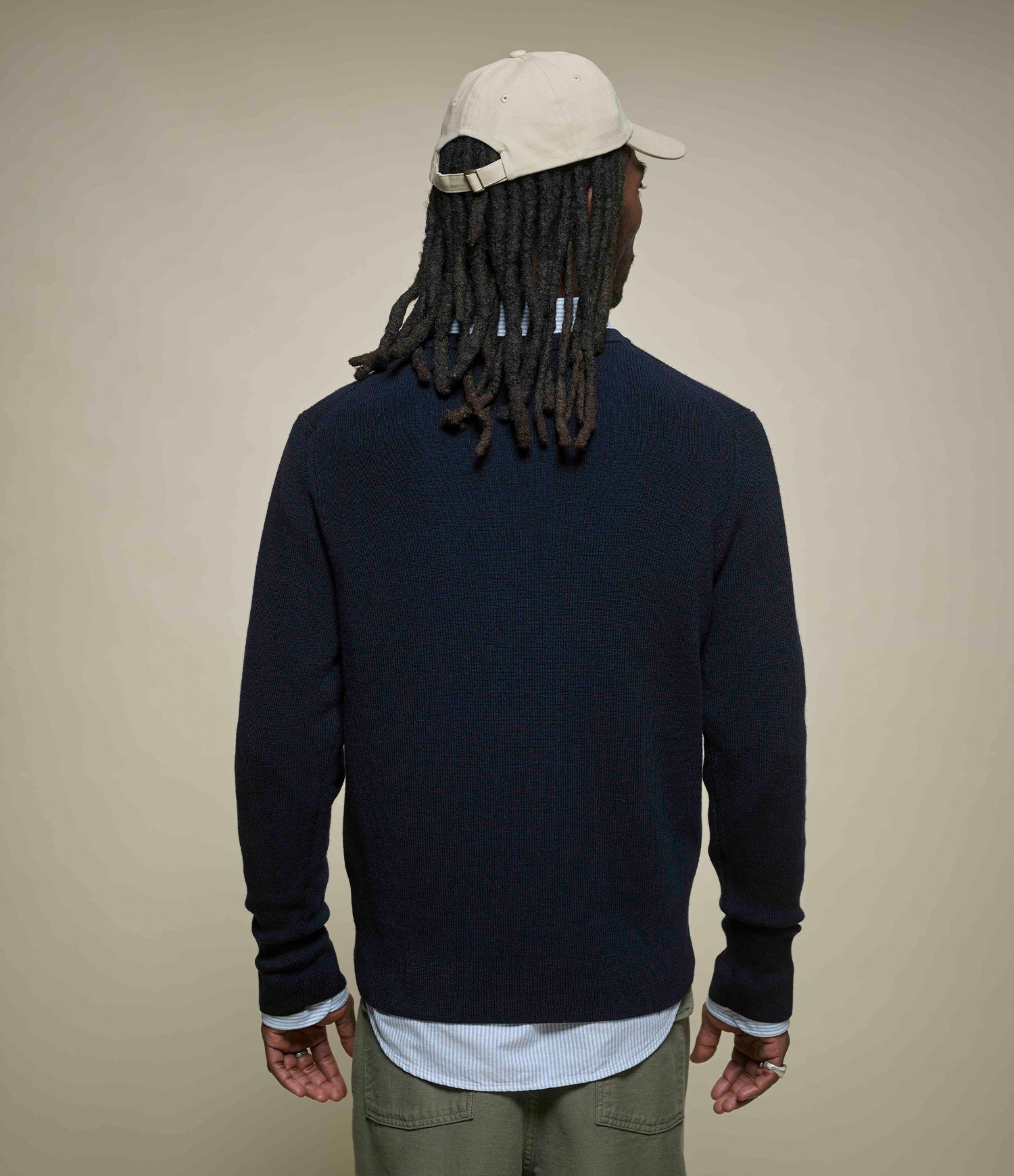 Person wearing a navy sweater, beige cap, and green pants on a beige background