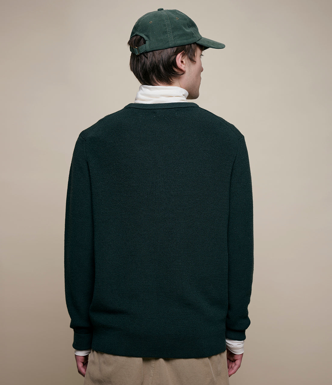 Person wearing a dark green sweater and cap on a beige background