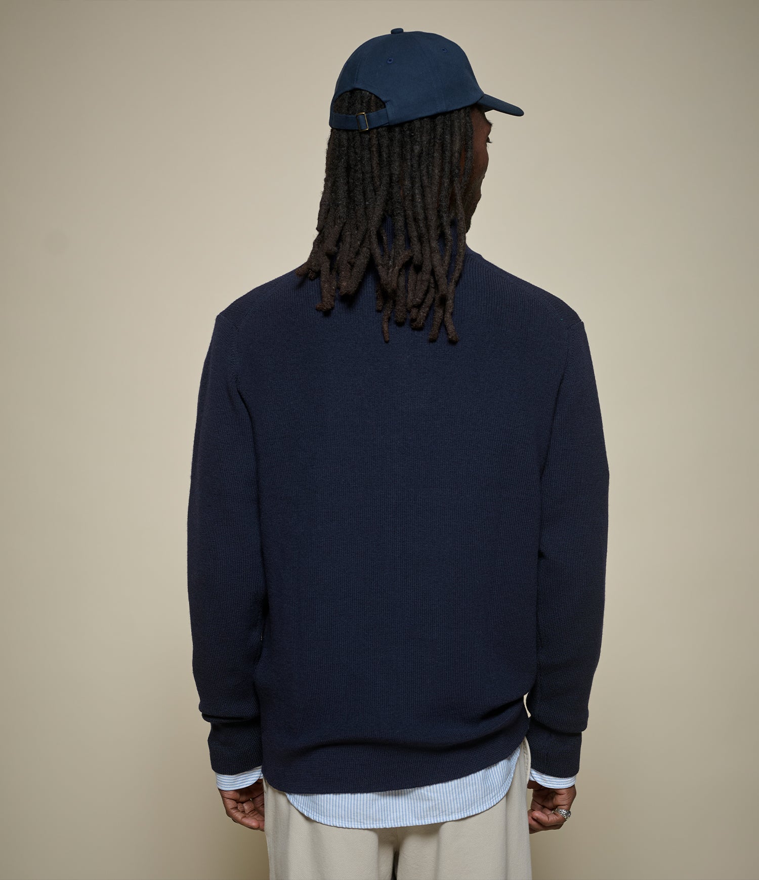 Person wearing a navy blue sweatshirt and cap on a beige background