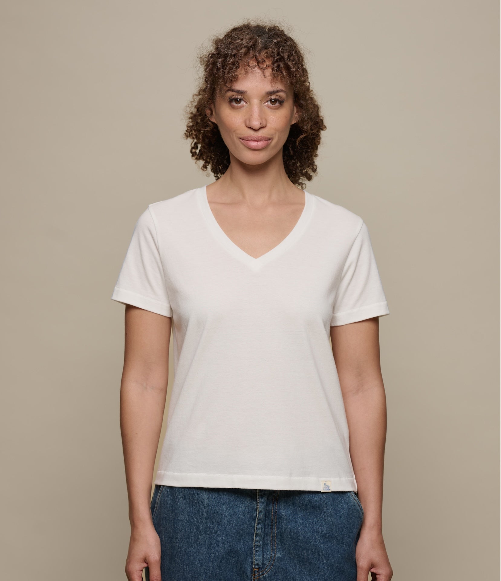 Woman wearing a plain white v-neck t-shirt against a beige background