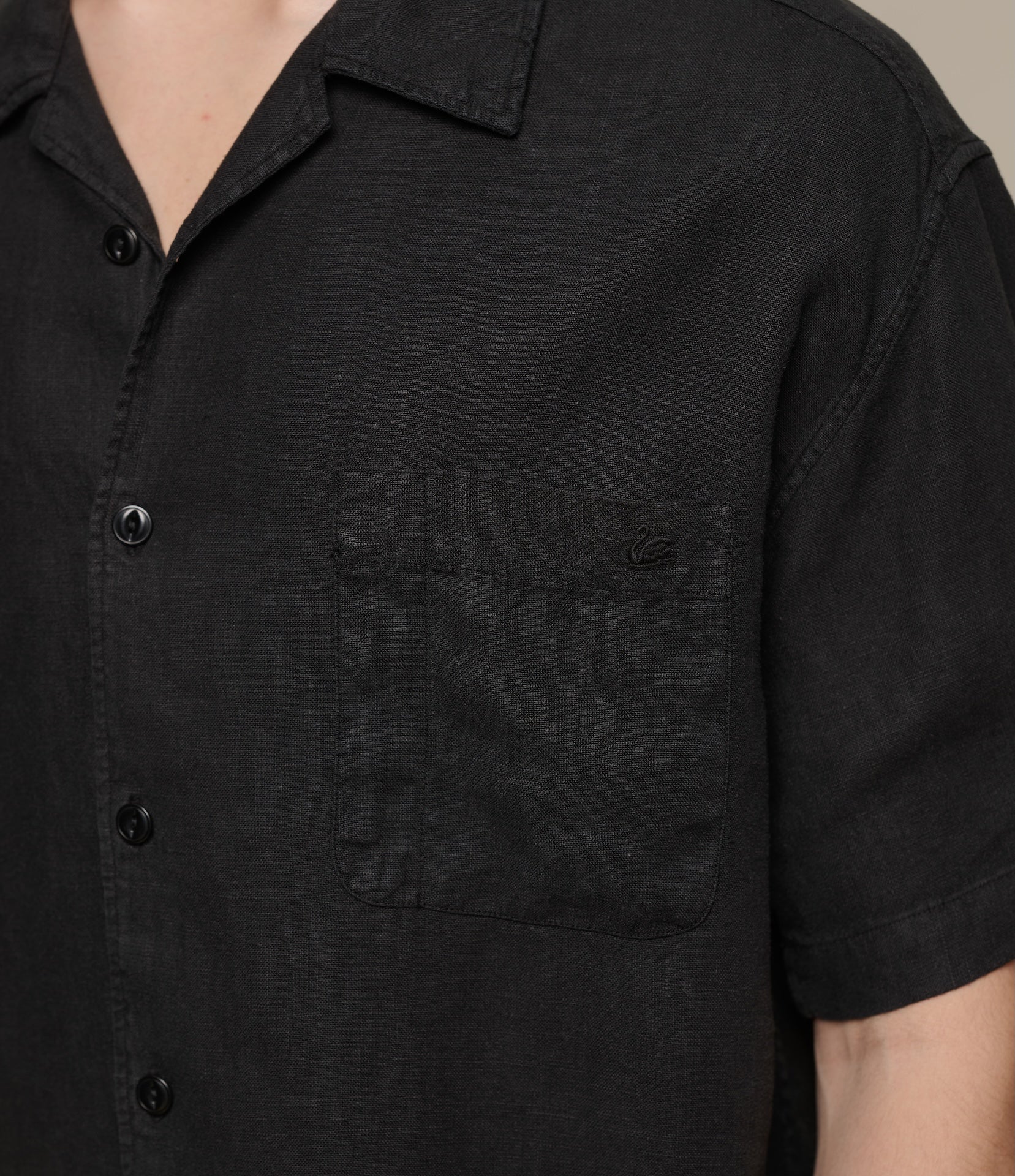 Black short-sleeve linen shirt with a pocket and swan embroidery on a neutral background
