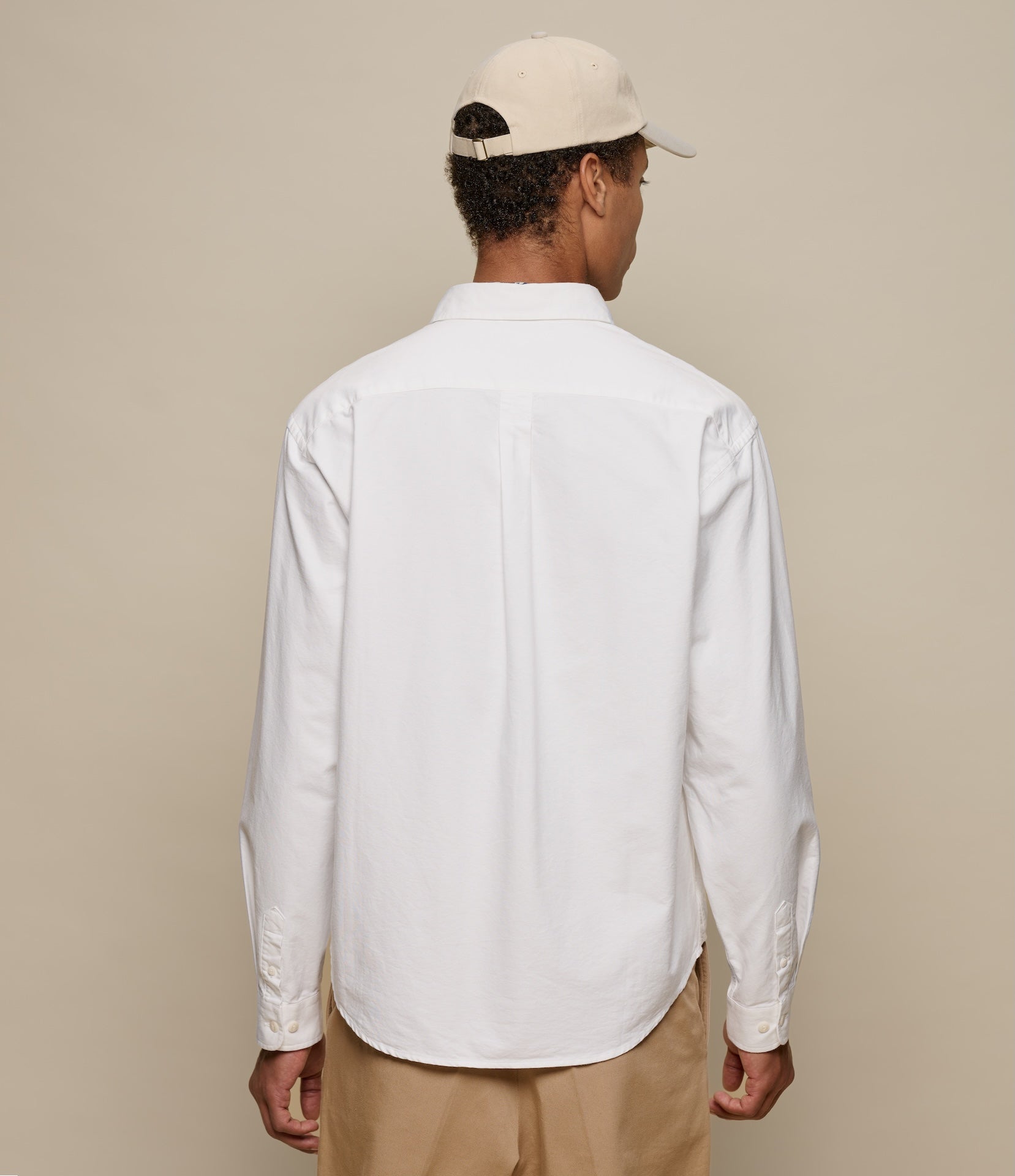 Person wearing a white oxford shirt and beige cap on a plain background