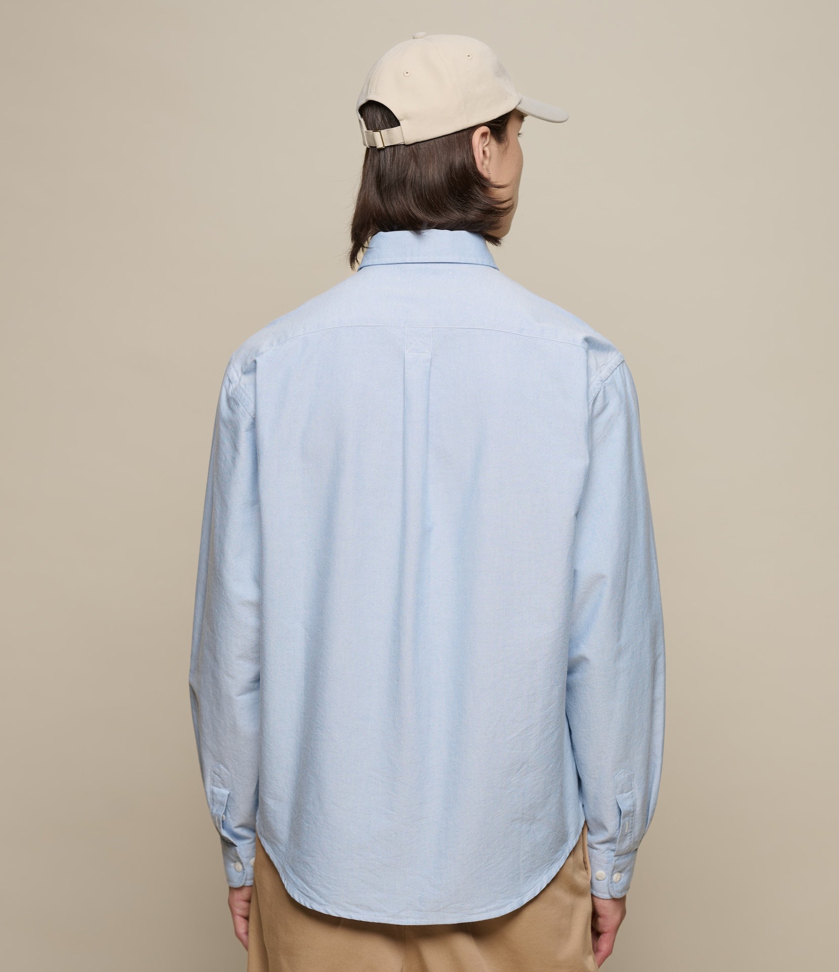 Person wearing a light blue shirt and beige cap on a beige background