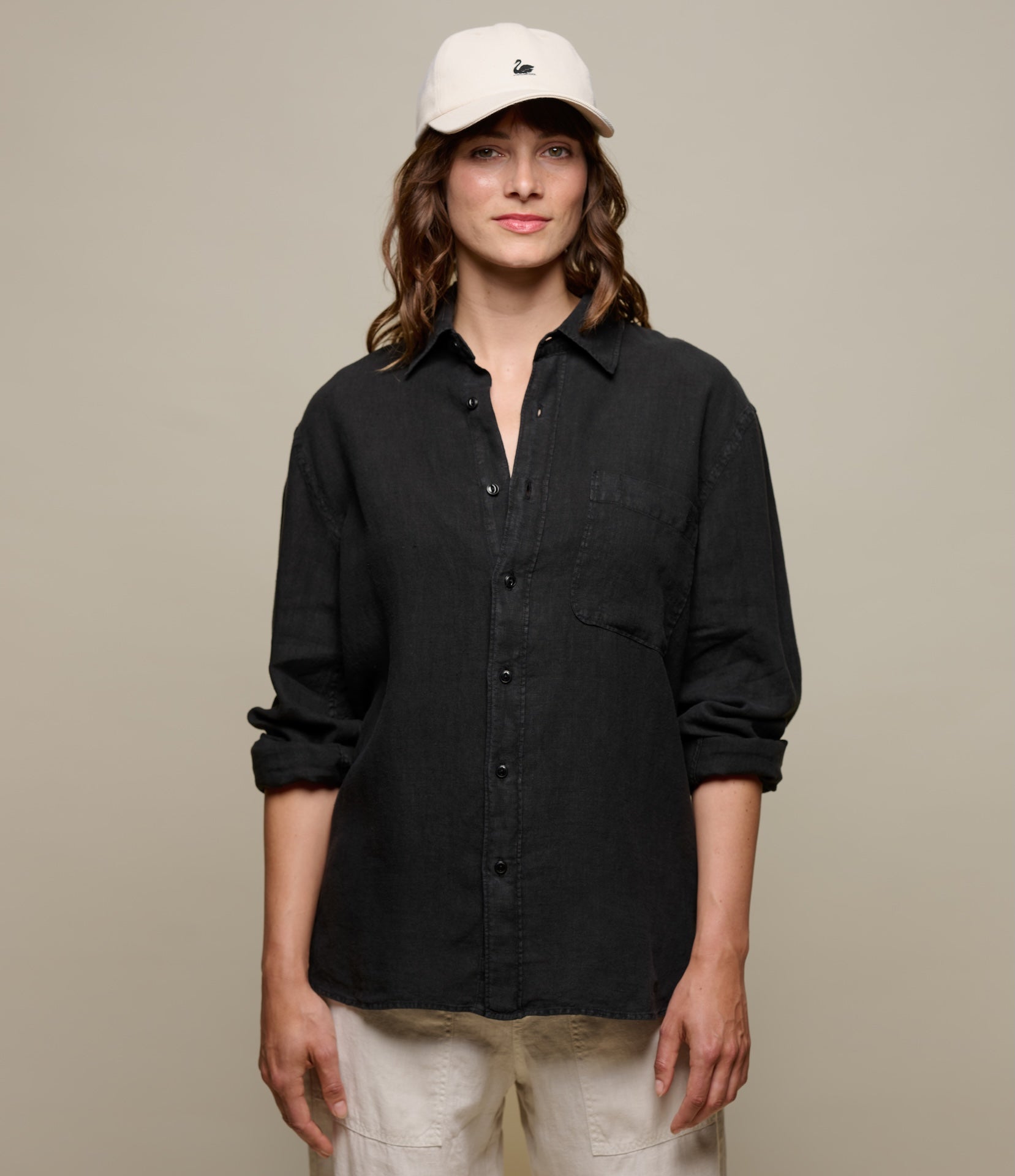Woman wearing a black button-up linen shirt and beige pants against a plain background