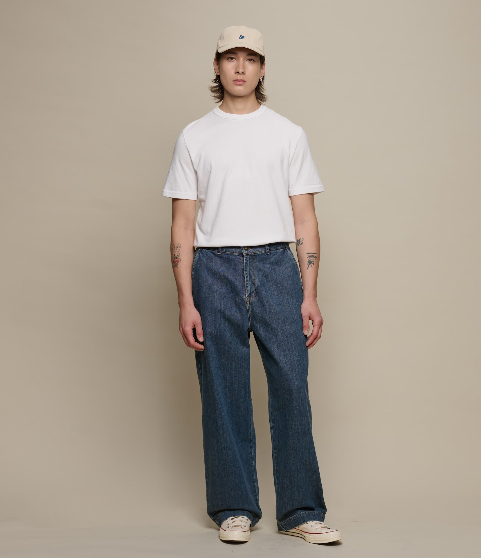 Person wearing a white t-shirt and blue jeans against a beige background