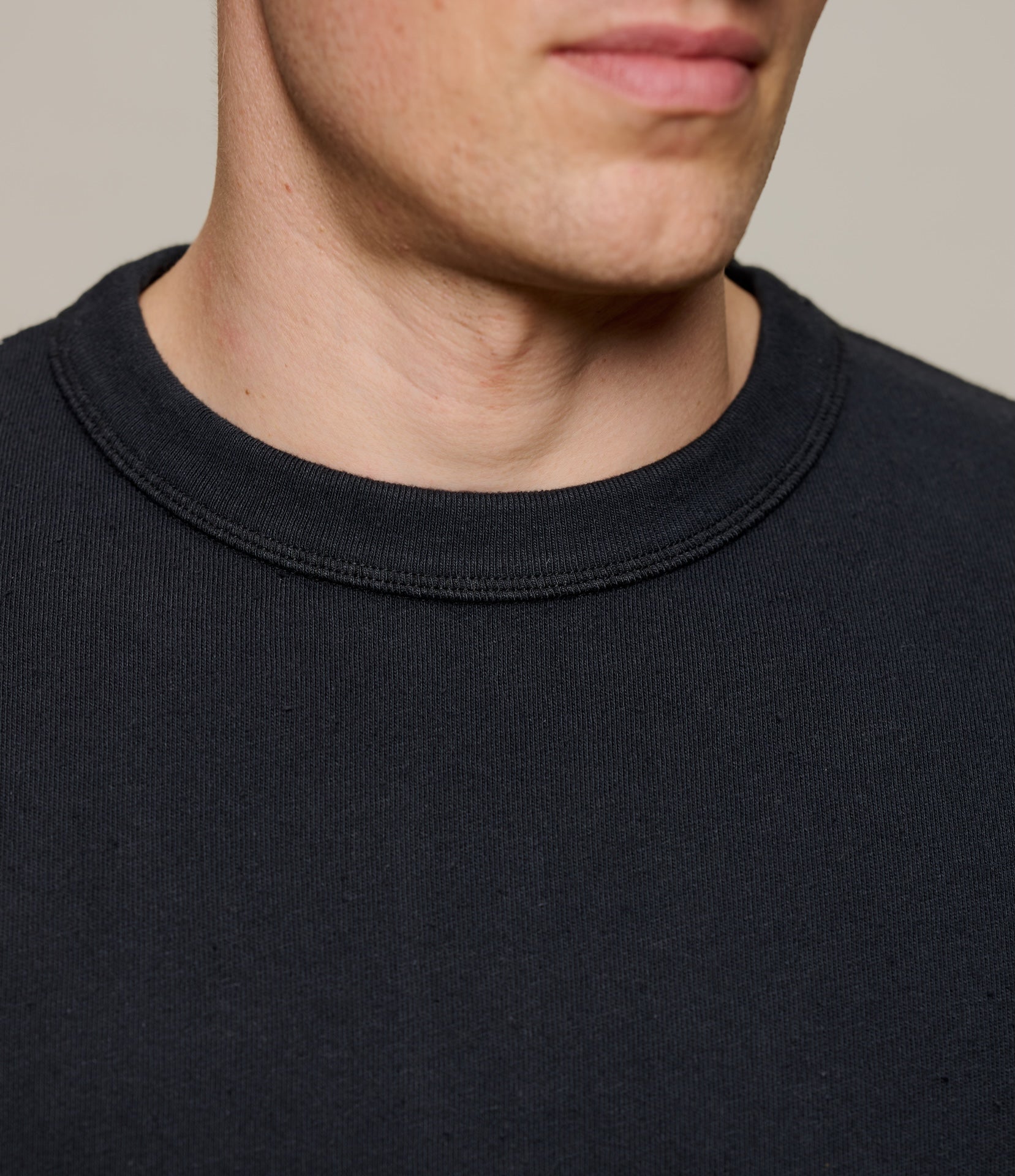 Close-up of a ribbed crew neck of a black T-shirt with a neutral background