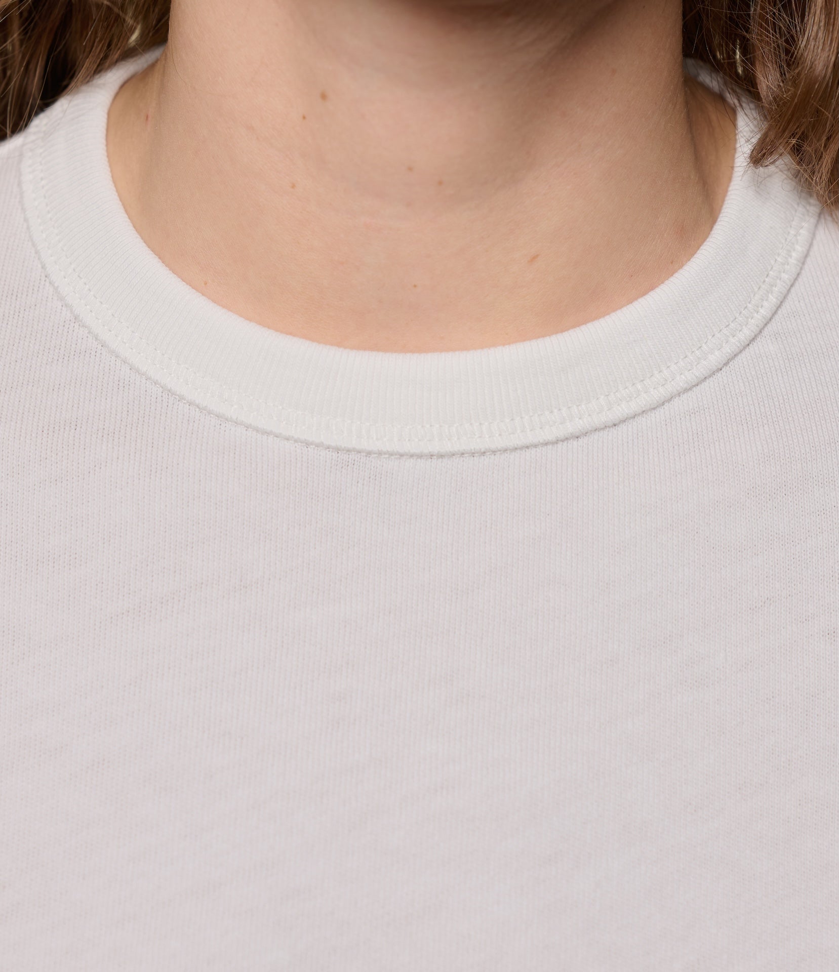 Close-up of a person wearing a plain white t-shirt with a focus on the ribbed neckline.