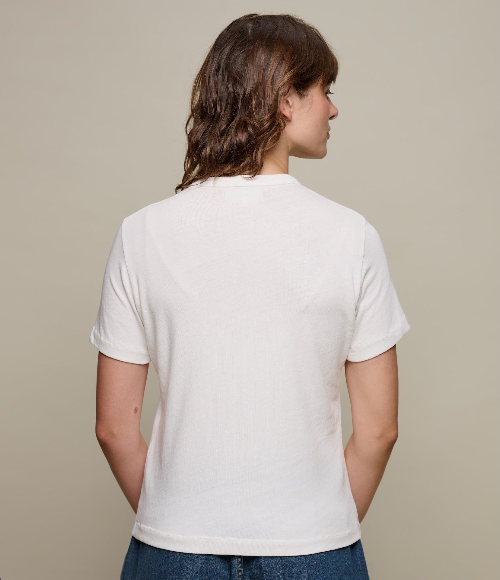 Person wearing a plain white t-shirt against a beige background