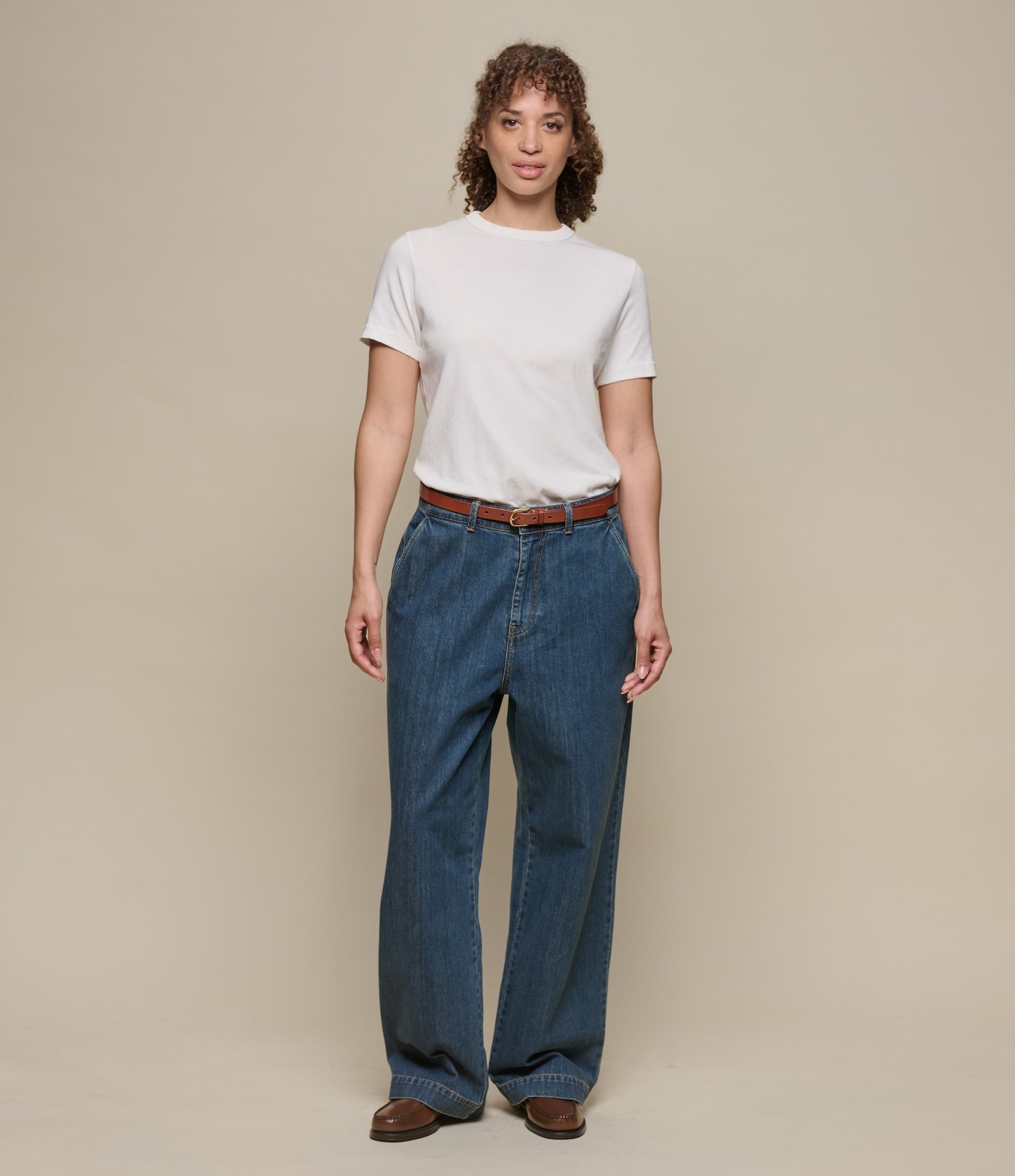 Person wearing a white t-shirt and blue jeans against a beige background