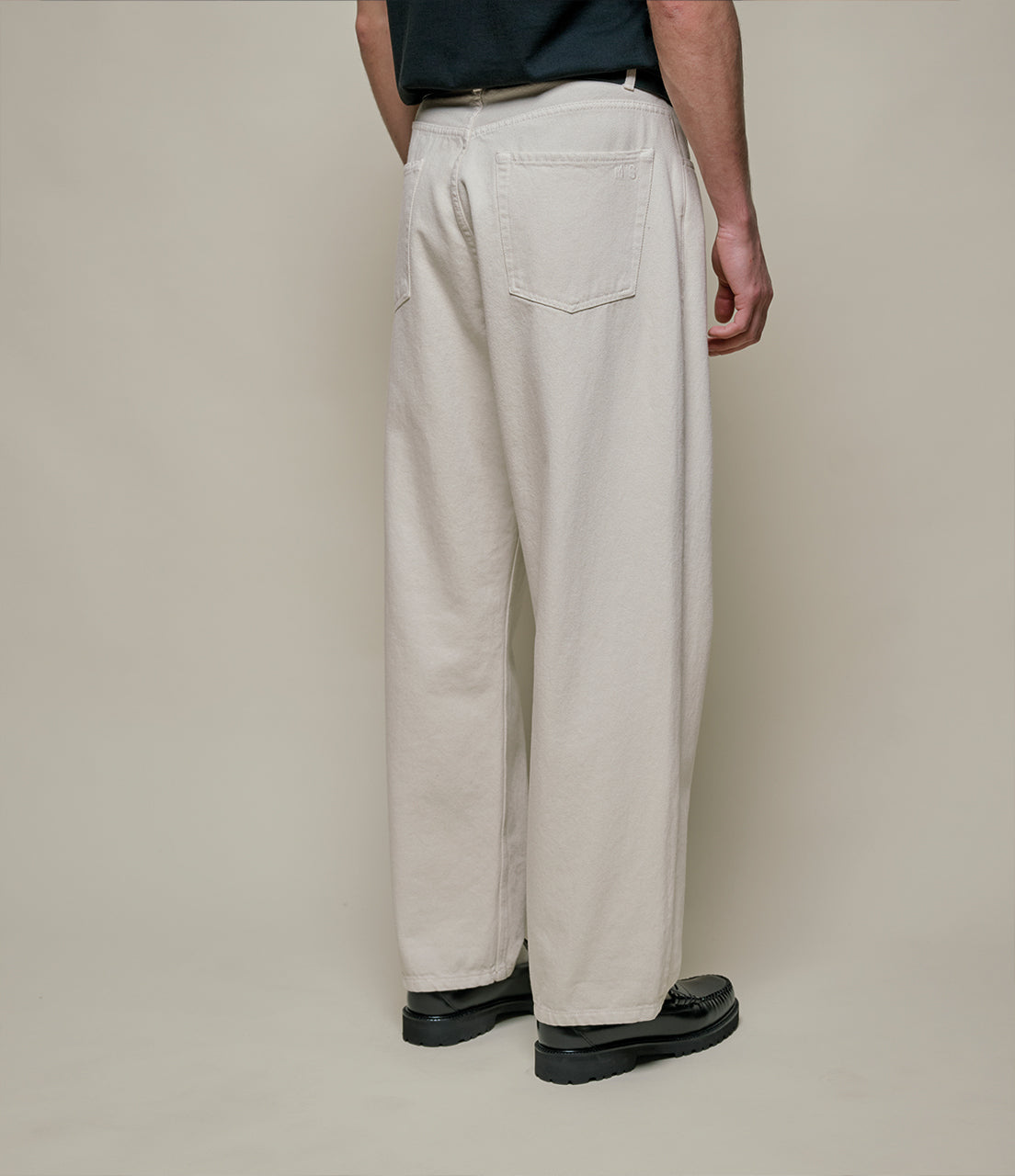 Person wearing beige pants and black shoes on a plain background