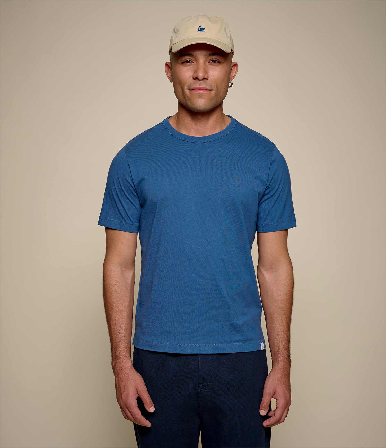 Man wearing an indigo blue t-shirt and beige cap on a beige background